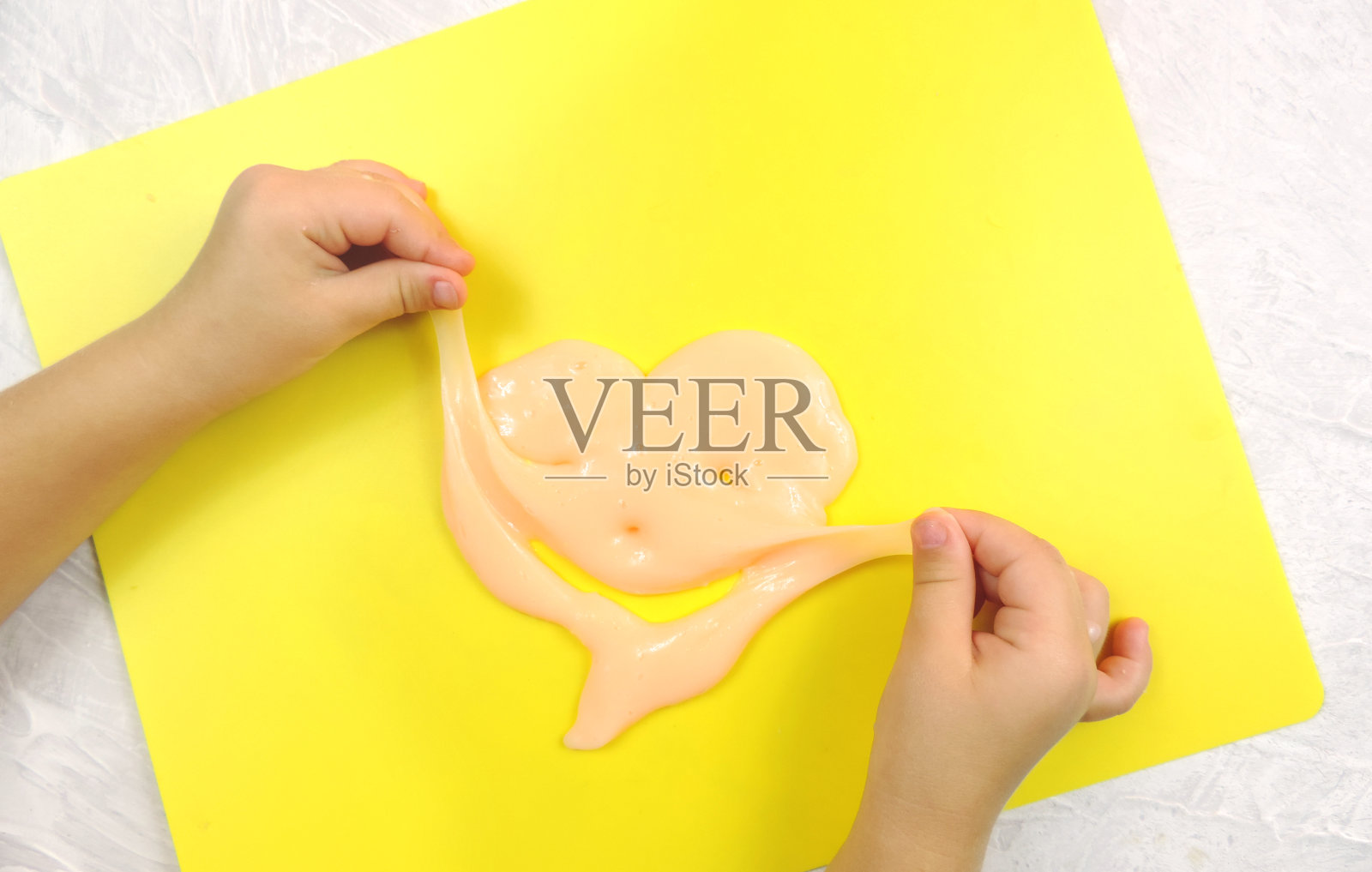 孩子的双手做了可笑的泥心,黄色的背景照片摄影图片