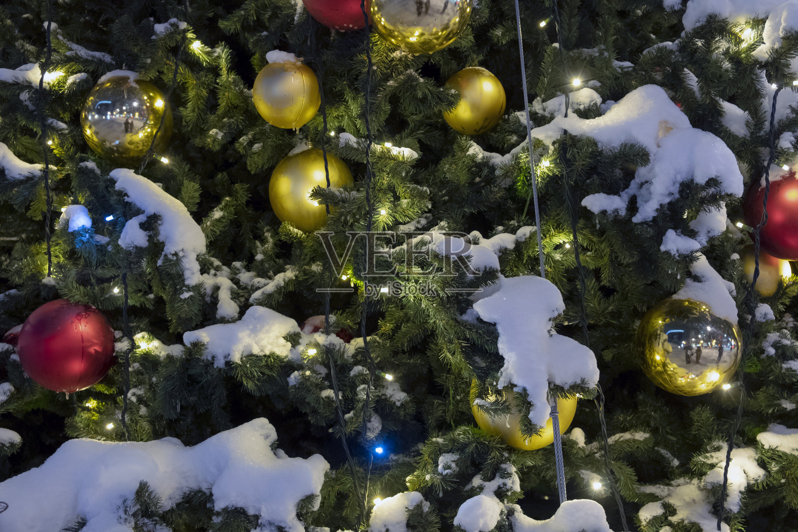 城市街道户外装饰圣诞树靠近红色和金色的小玩意儿和花环在晚上。照片摄影图片
