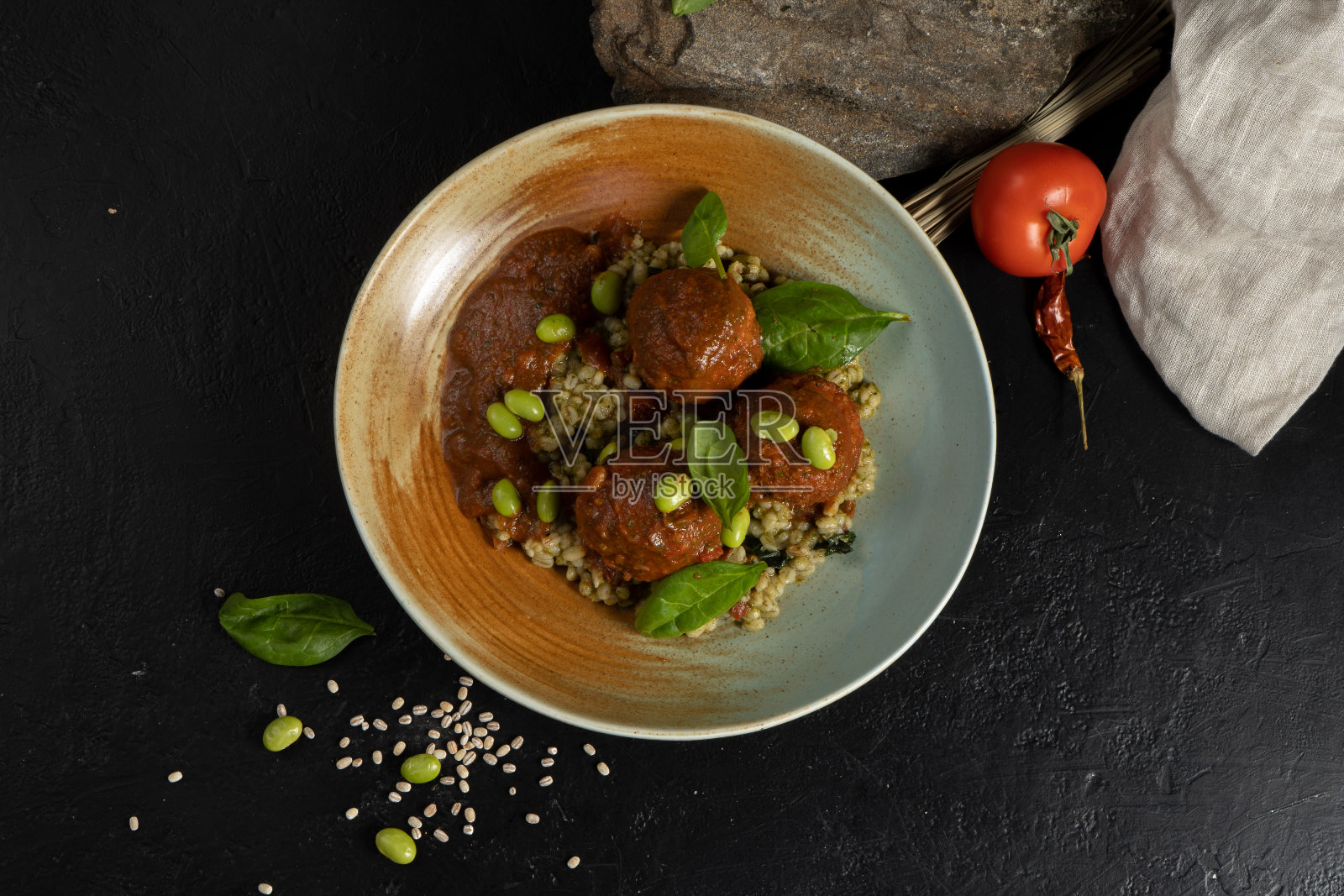 大麦粥丸子,番茄酱,豆子和莴苣。黑色的厨房石桌上放着一盘热腾腾的谷物和豆类。照片摄影图片