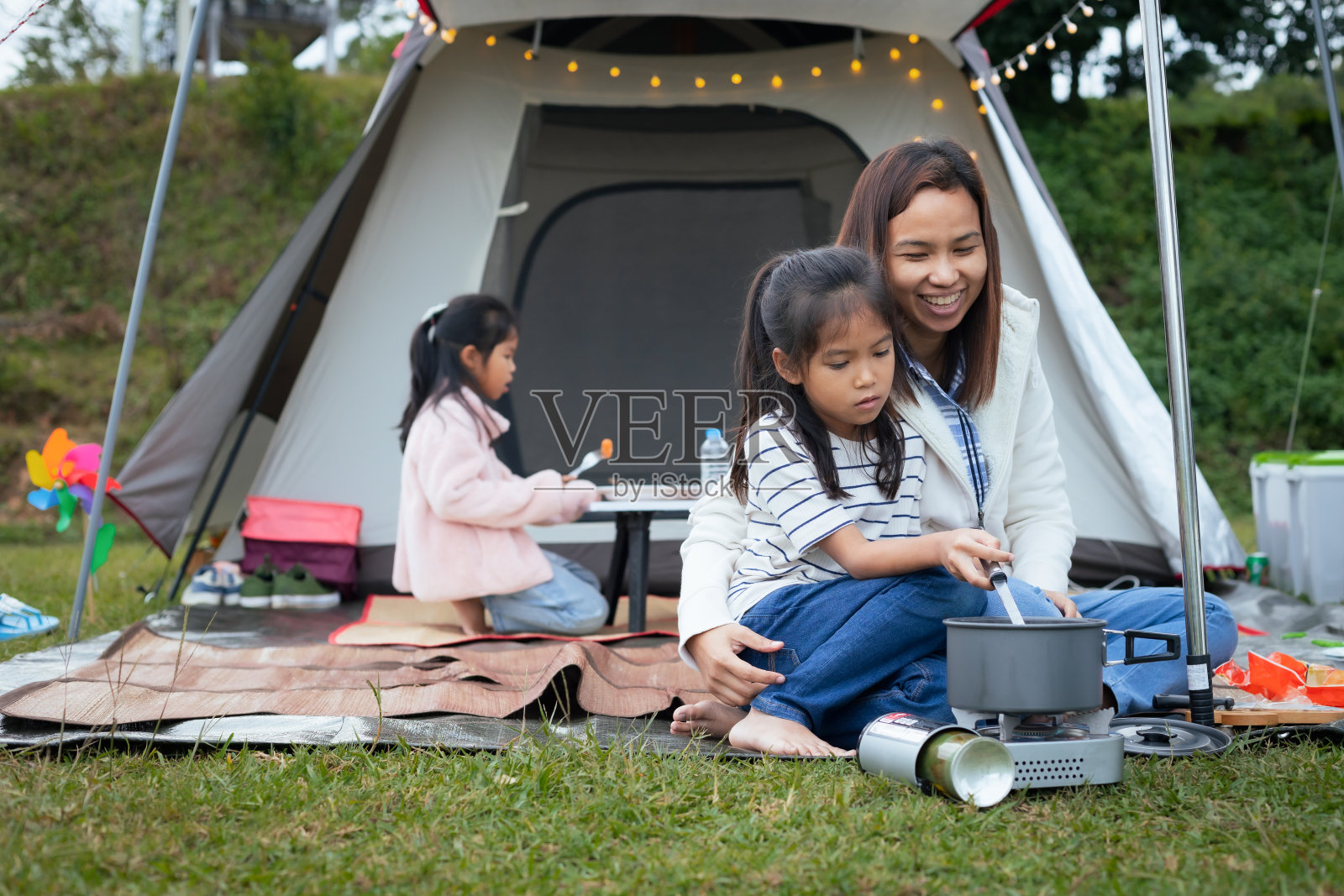 可爱的亚洲女孩有乐趣,帮助她的母亲烹饪帐篷外,而露营与家人。照片摄影图片