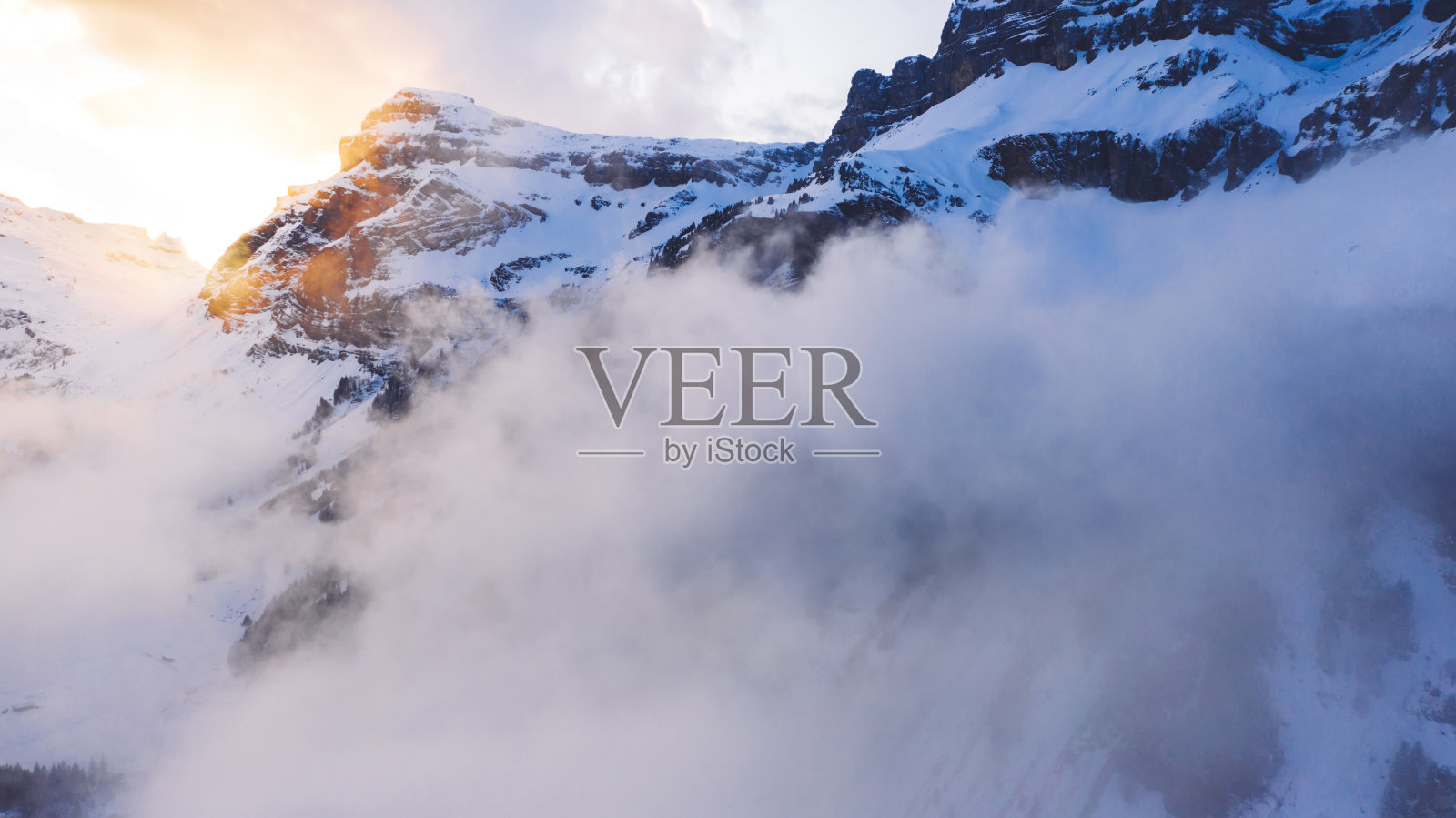 令人叹为观止的冰天雪地的岩石和天空与日落和云野北部景观,鸟瞰高山和冰雪山顶在冬季度假胜地照片摄影图片