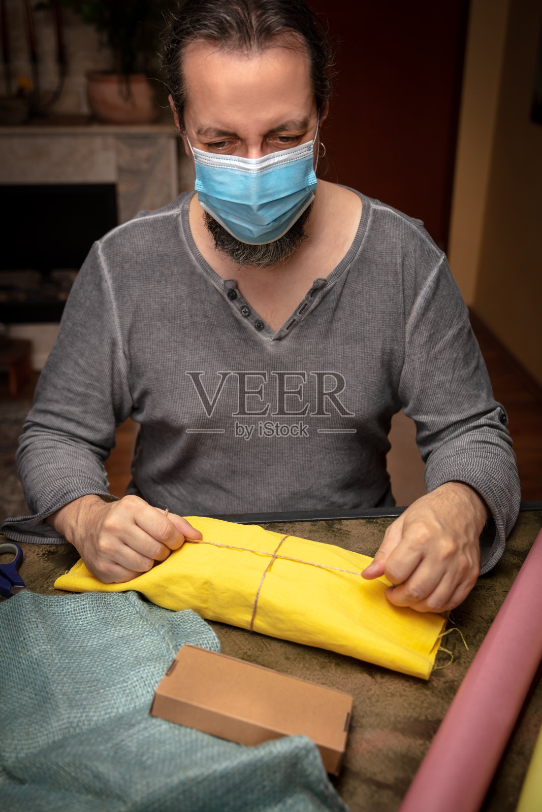 男子包装圣诞或生日礼物并佩戴外科口罩、概念冠状病毒和covid-19照片摄影图片