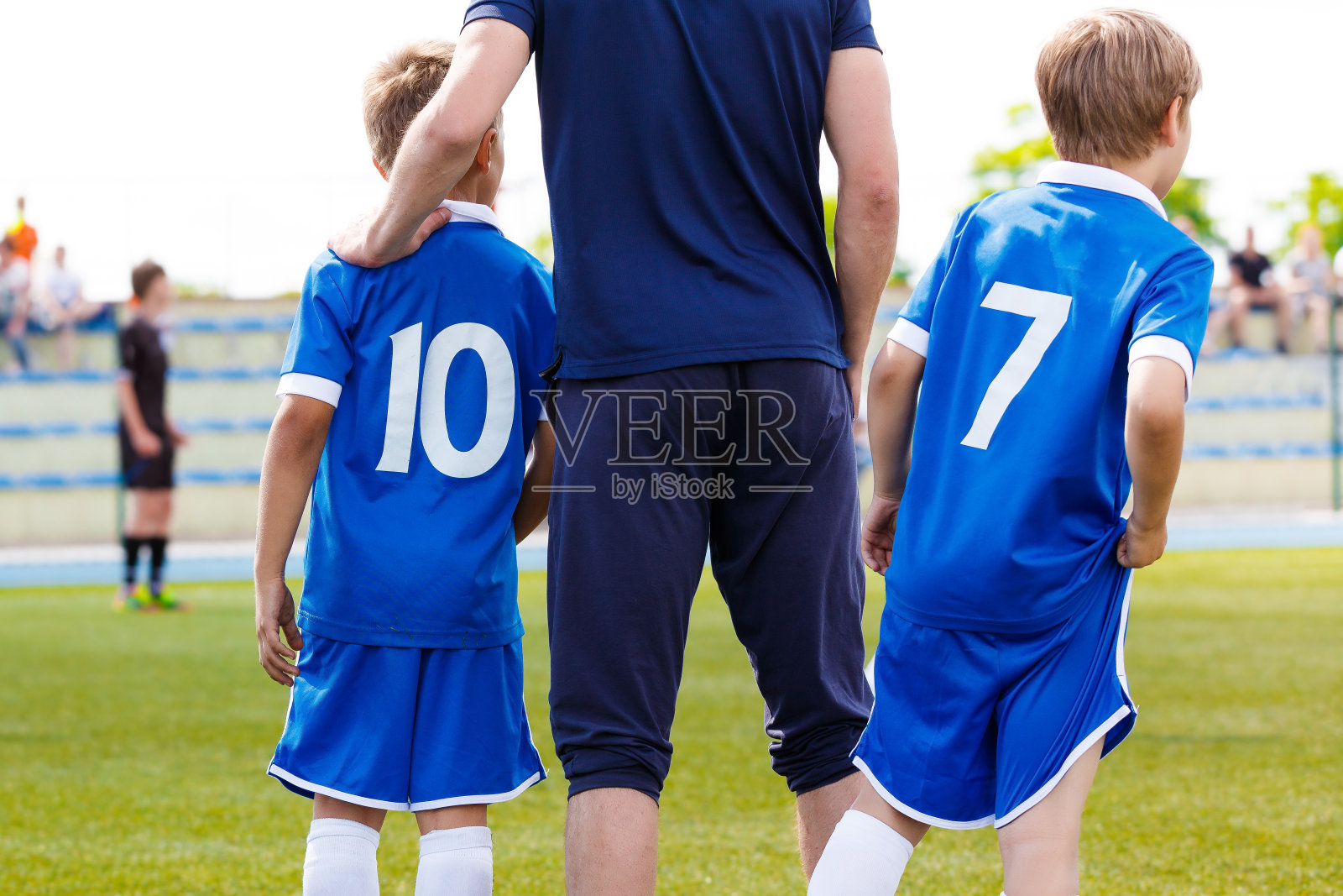 足球男孩与年轻教练在锦标赛上。教练把手放在球员肩膀上换人。学校足球队的孩子们照片摄影图片
