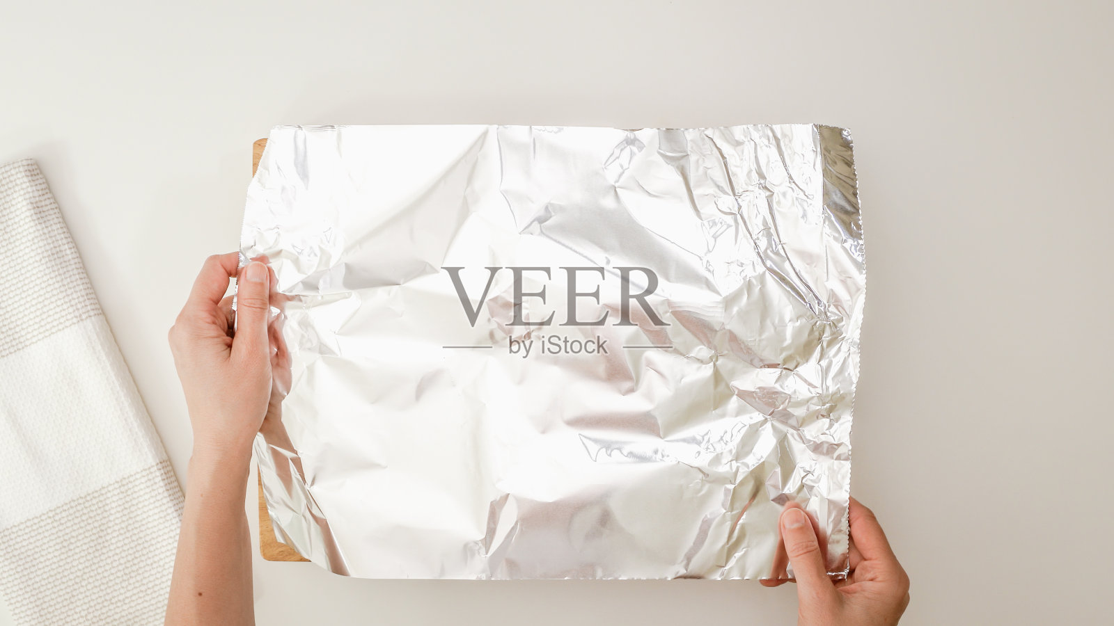 一次性烤盘放在餐桌上,平放。女人用铝箔把锅盖上。一步一步的烘烤过程照片摄影图片