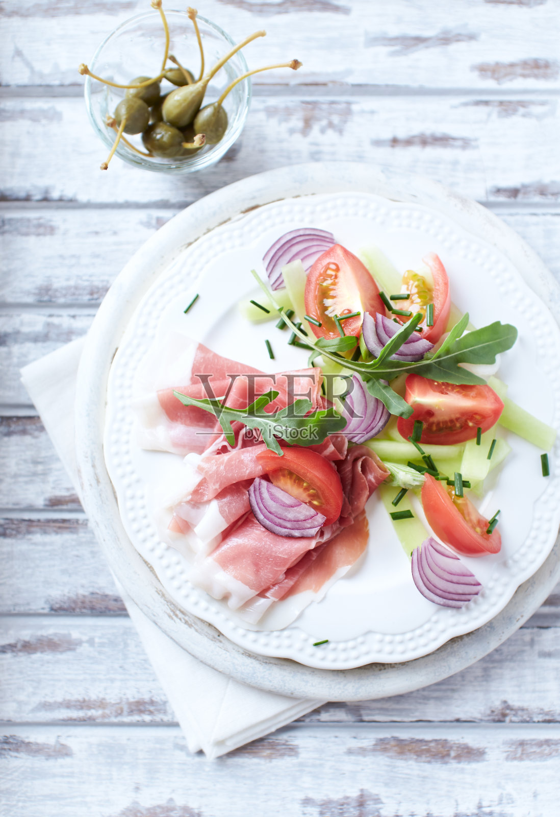 一盘加番茄和芝麻菜的熏火腿。明亮的木制背景。前视图。照片摄影图片