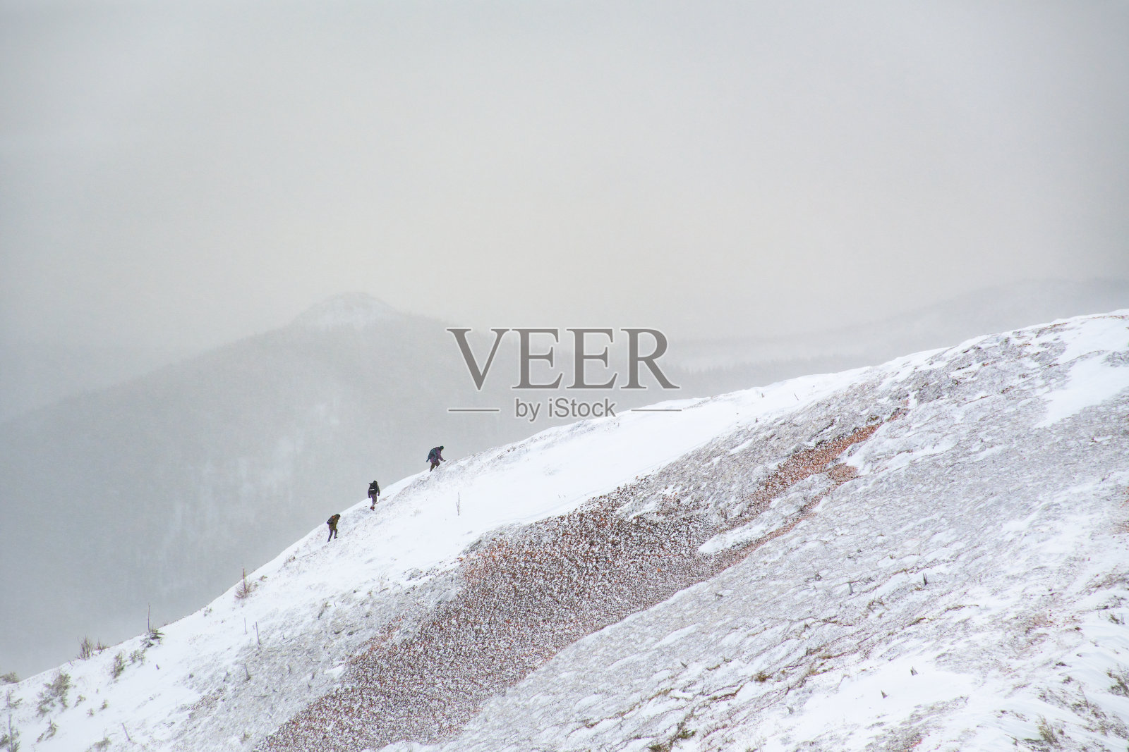 三个徒步旅行者在雪中爬上了山脊的顶峰照片摄影图片