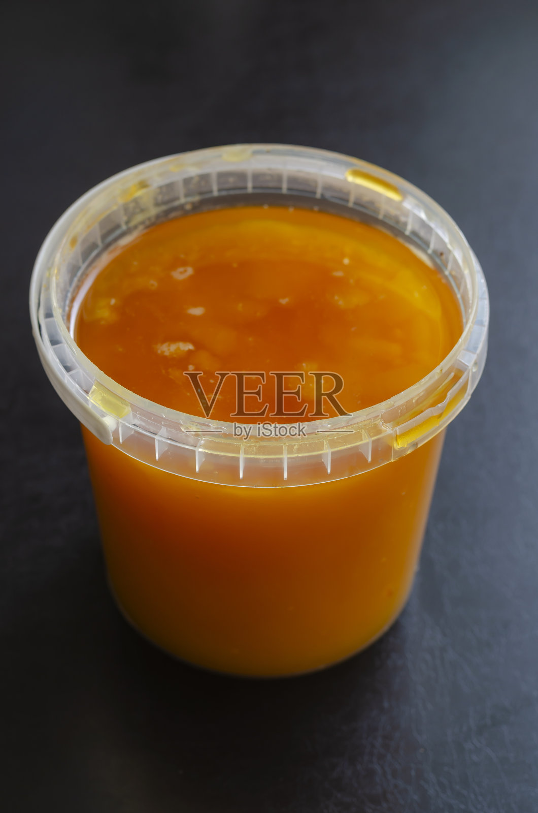 有机黄色蜜蜂蜂蜜在一个圆柱形塑料容器在黑色的背景。照片摄影图片