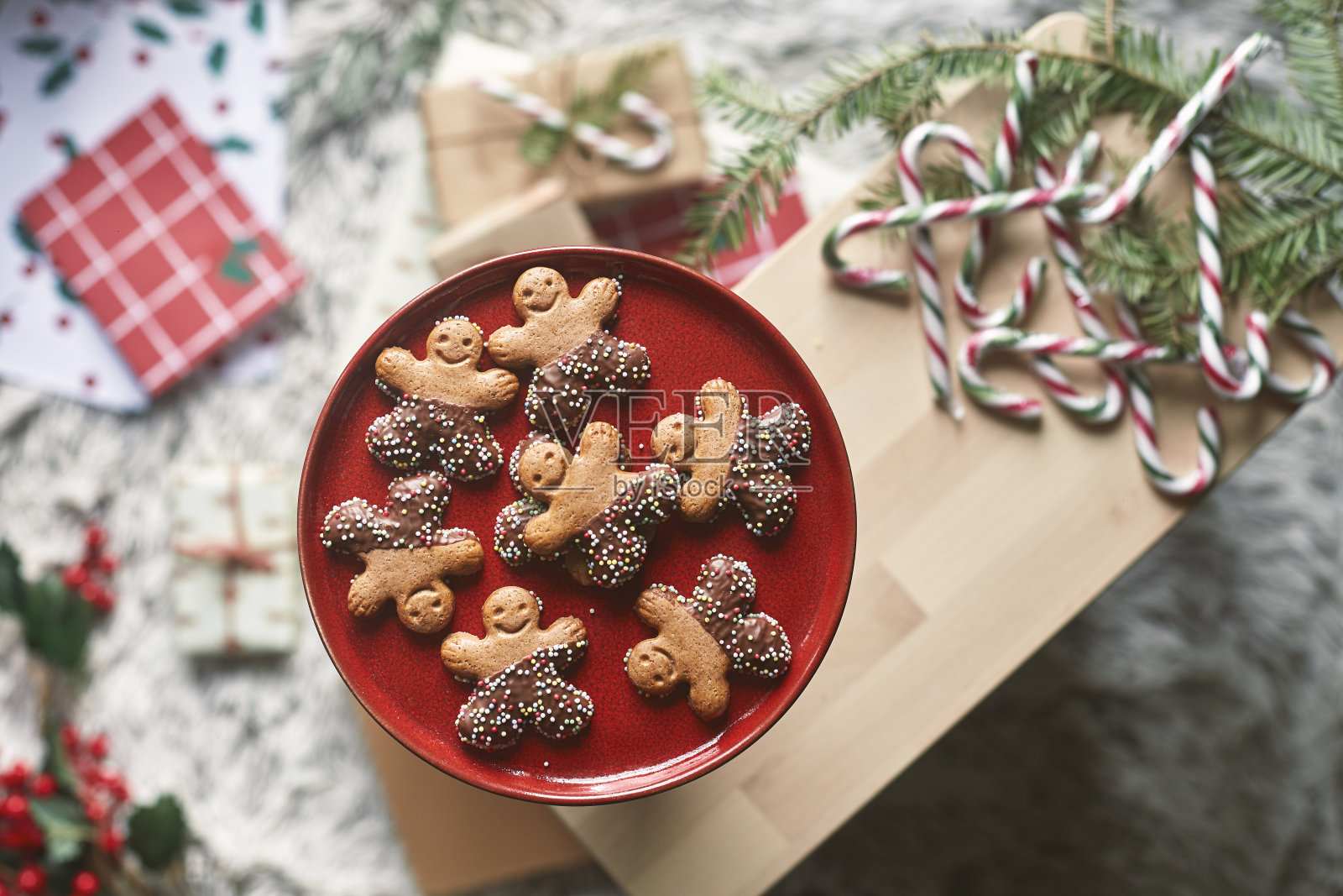 红色盘子里有姜饼、巧克力和娃娃形状的八角。围绕着礼物,槲寄生,冷杉树叶和糖果棒照片摄影图片