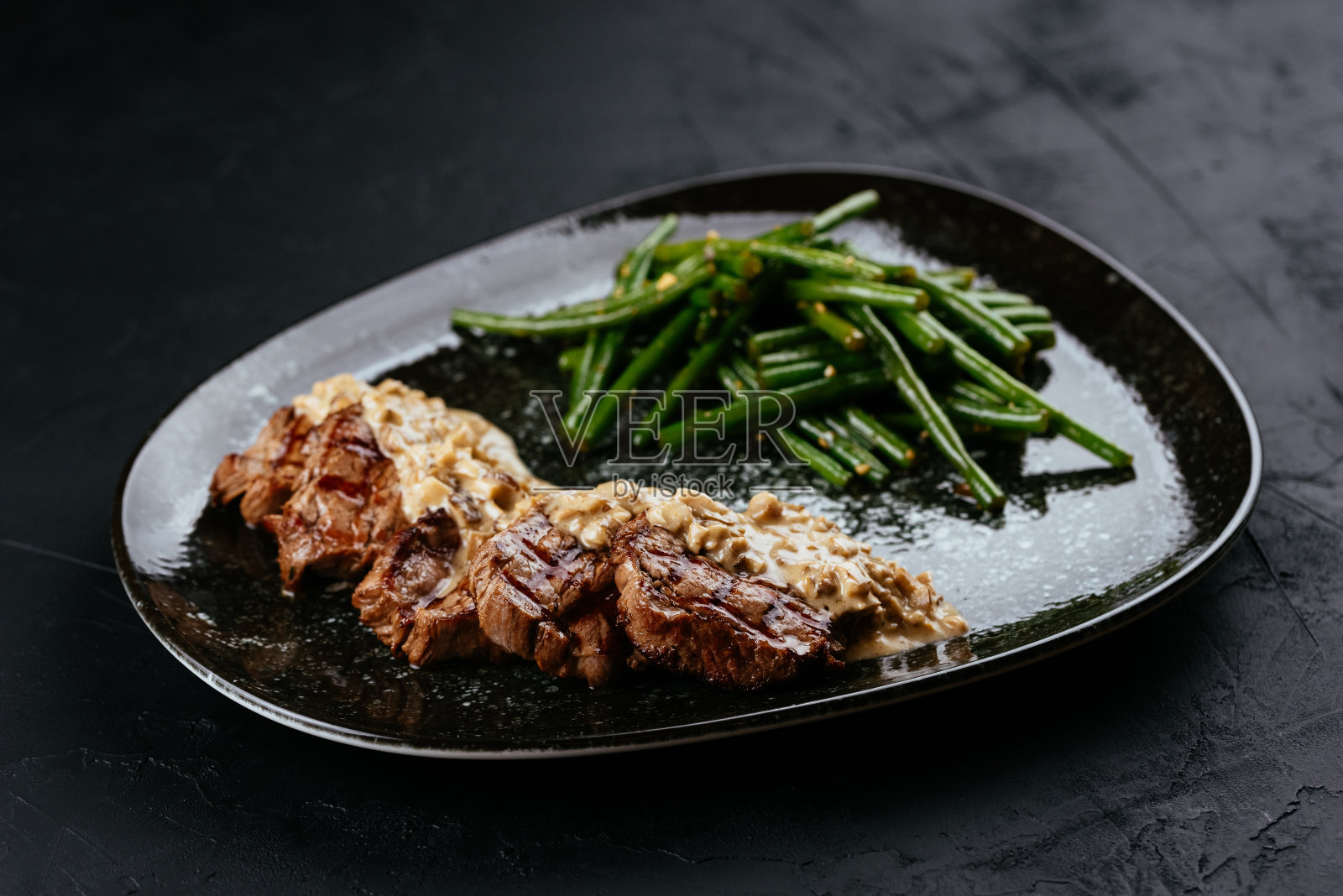 黑色背景上的大理石纹牛肉牛排配蔬菜和酱汁照片摄影图片