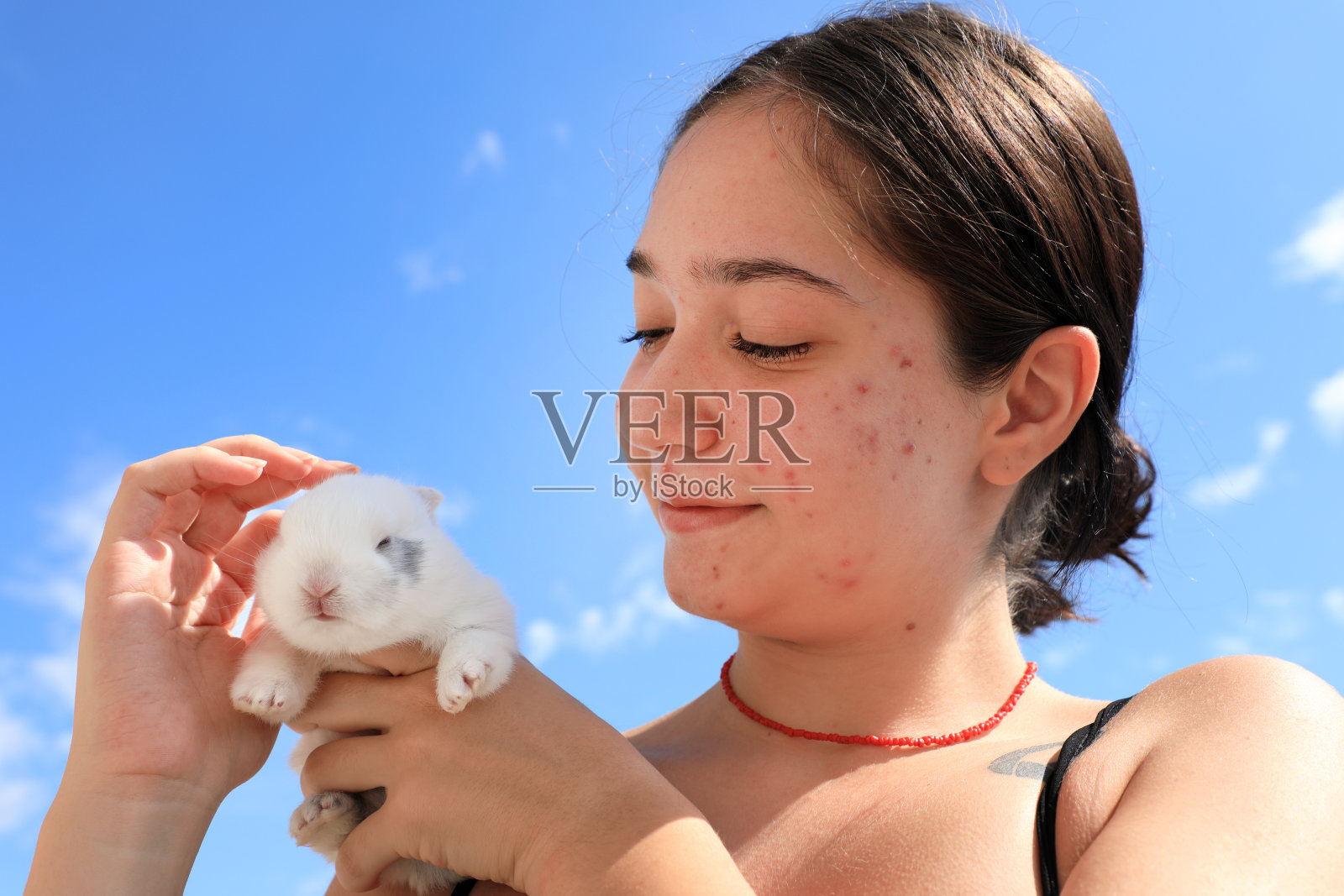 一个十几岁的女孩在晴朗的天空中抱着兔子宝宝照片摄影图片
