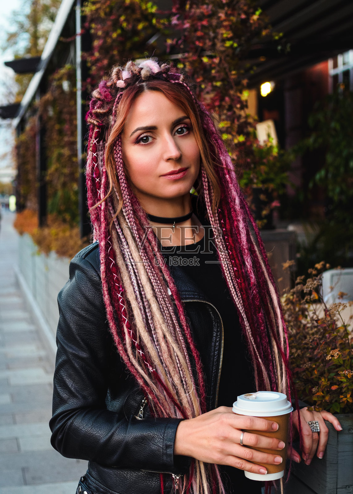 这个自信的女人留着粉红色的长发辫发型,穿着黑色的衣服看着镜头,拍摄于秋天的户外照片摄影图片