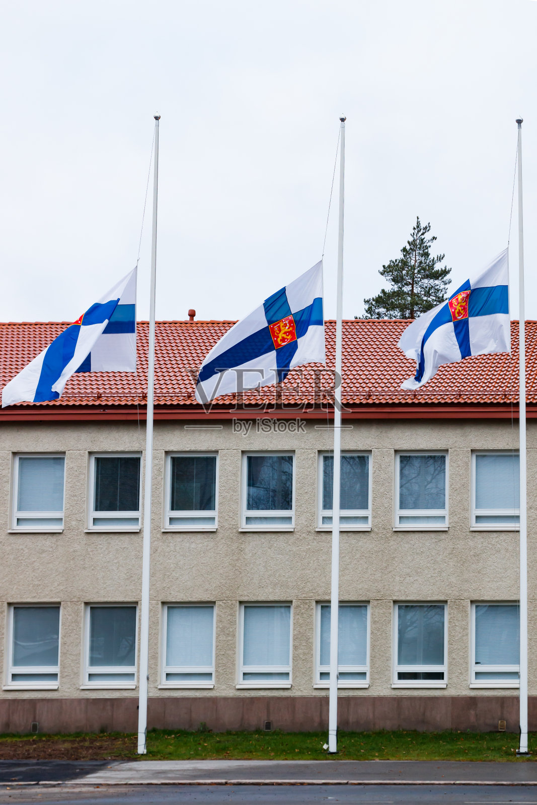 在阴天的秋日,三面芬兰国旗下半旗致哀照片摄影图片