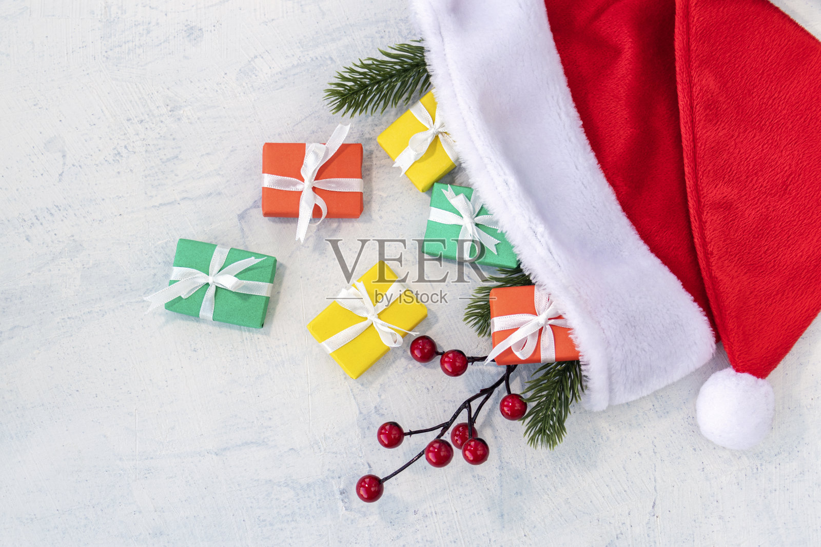 五颜六色的圣诞礼物放在圣诞老人的帽子里放在白色的水泥桌上。概念圣诞快乐,新年快乐。副本的空间。照片摄影图片