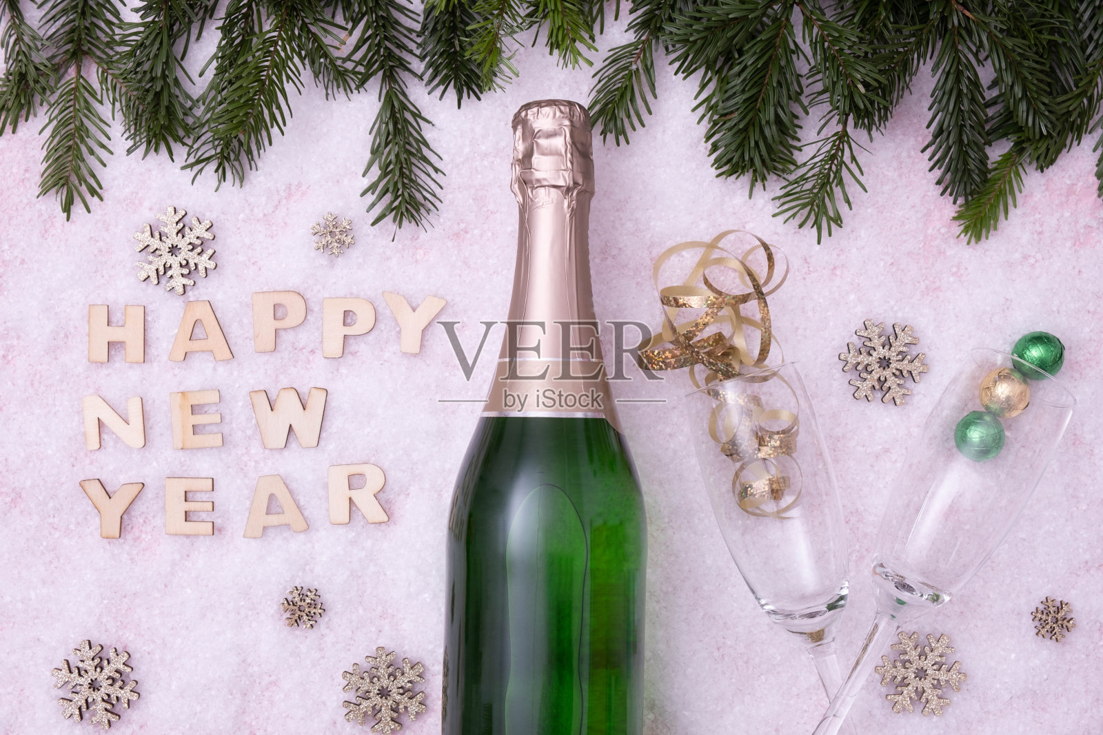 节日的桌子上放着满满一瓶香槟,旁边写着:“新年快乐”,背景是雪景照片摄影图片