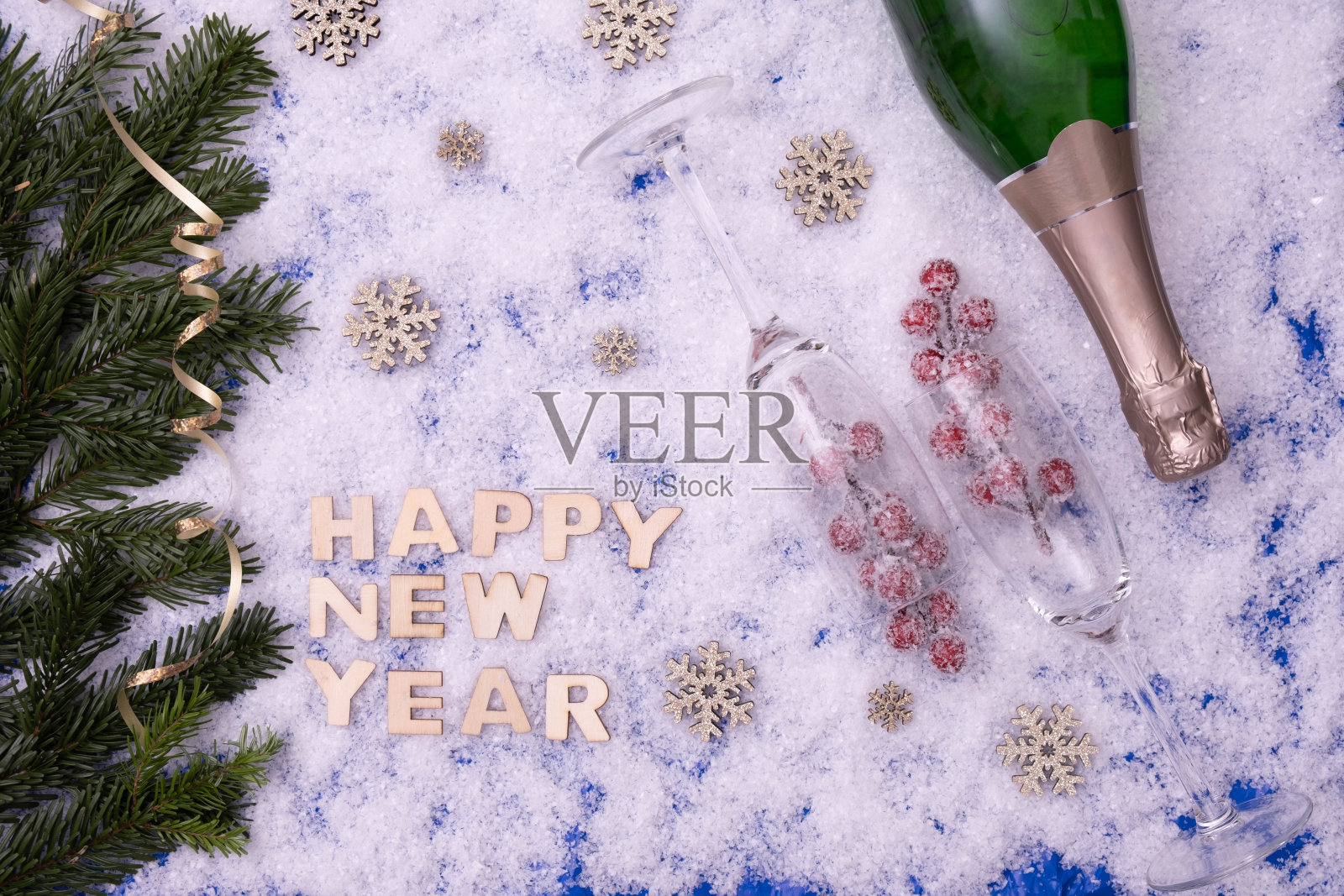 喜庆的餐桌上放着香槟、糖果、云杉树枝、酒杯,旁边写着“新年快乐”,背景是雪景照片摄影图片
