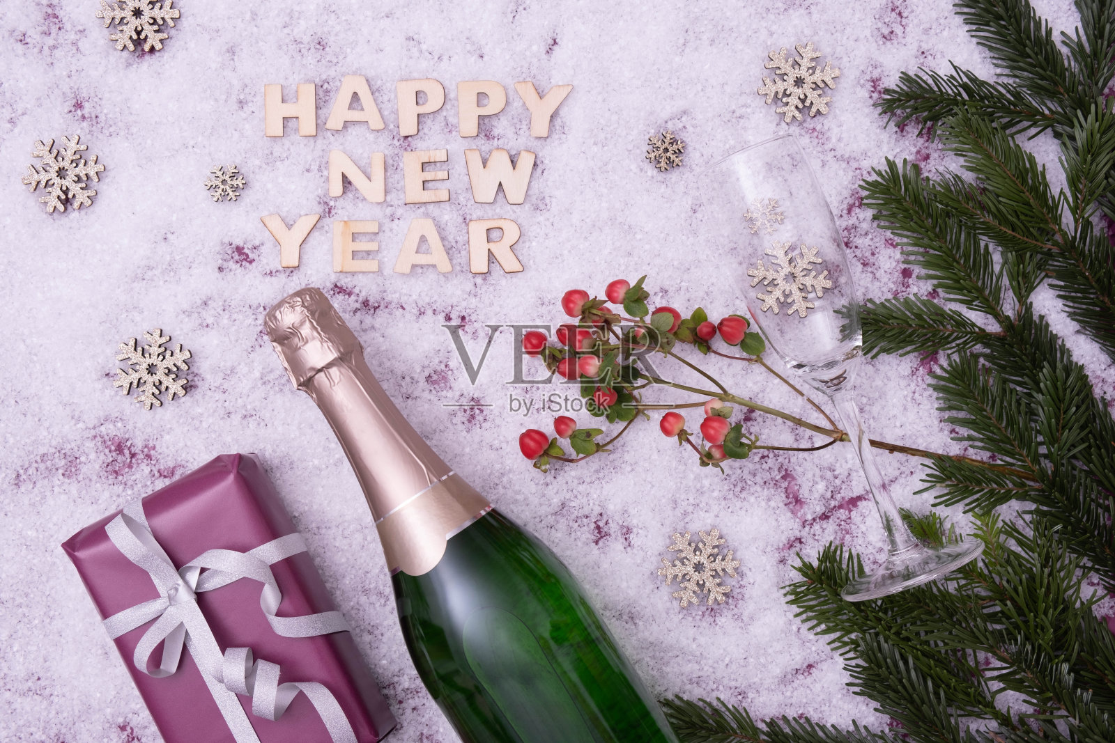 节日的餐桌上摆放着云杉树枝、礼物、糖果、香槟和酒杯,旁边写着“新年快乐”,背景是雪景照片摄影图片