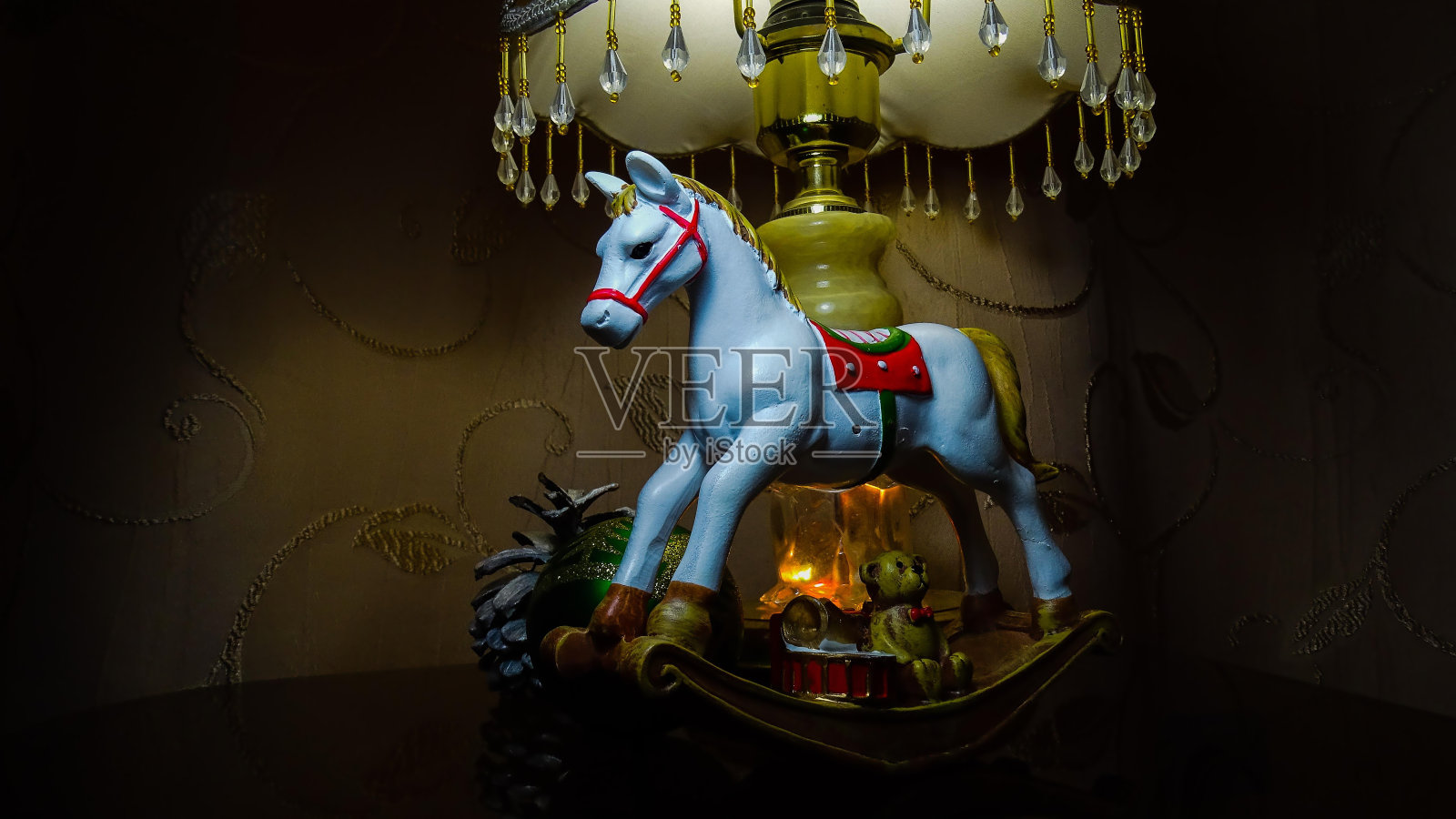 Cristmas礼物。一个玩具,一个白色的摇木马,小礼物,一个绿色的球,一个松果。夜灯。金色织物上的区域灯。照片摄影图片