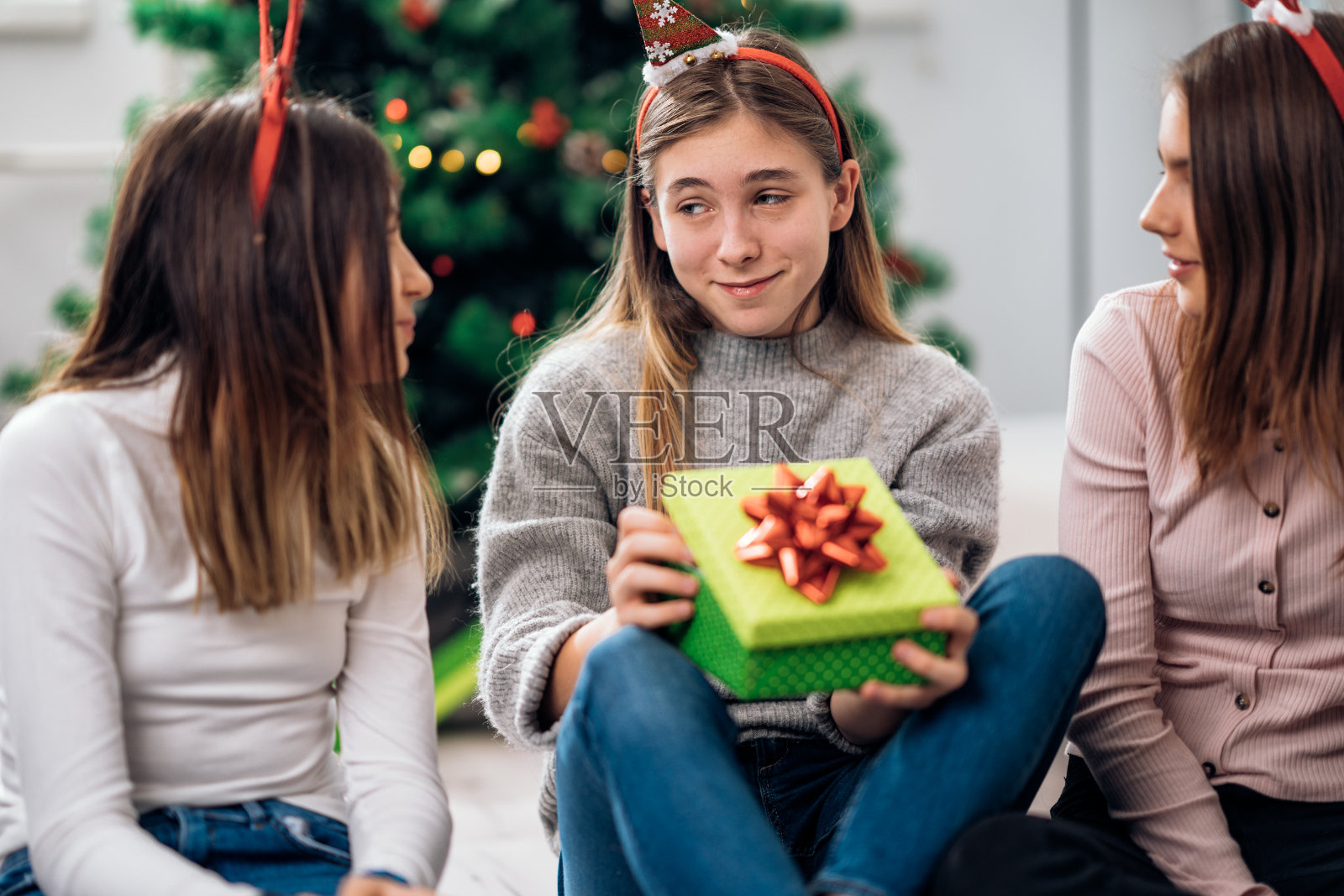 和朋友在圣诞树前打开礼物的女孩照片摄影图片