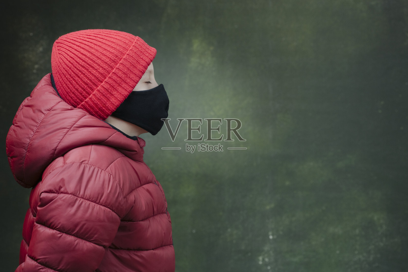 男孩戴着防冠状病毒的黑色安全口罩,穿着冬季夹克和红色帽子。侧视图。Covid-19在全球爆发照片摄影图片