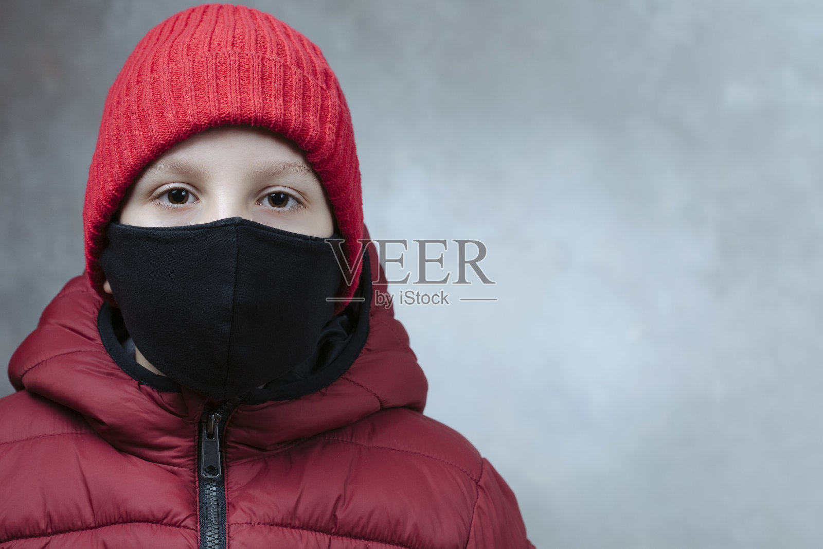 男孩戴着冬季防护冠状病毒的安全黑色口罩,红色夹克和红色帽子,背景受损。特写。Covid-19在全球爆发照片摄影图片