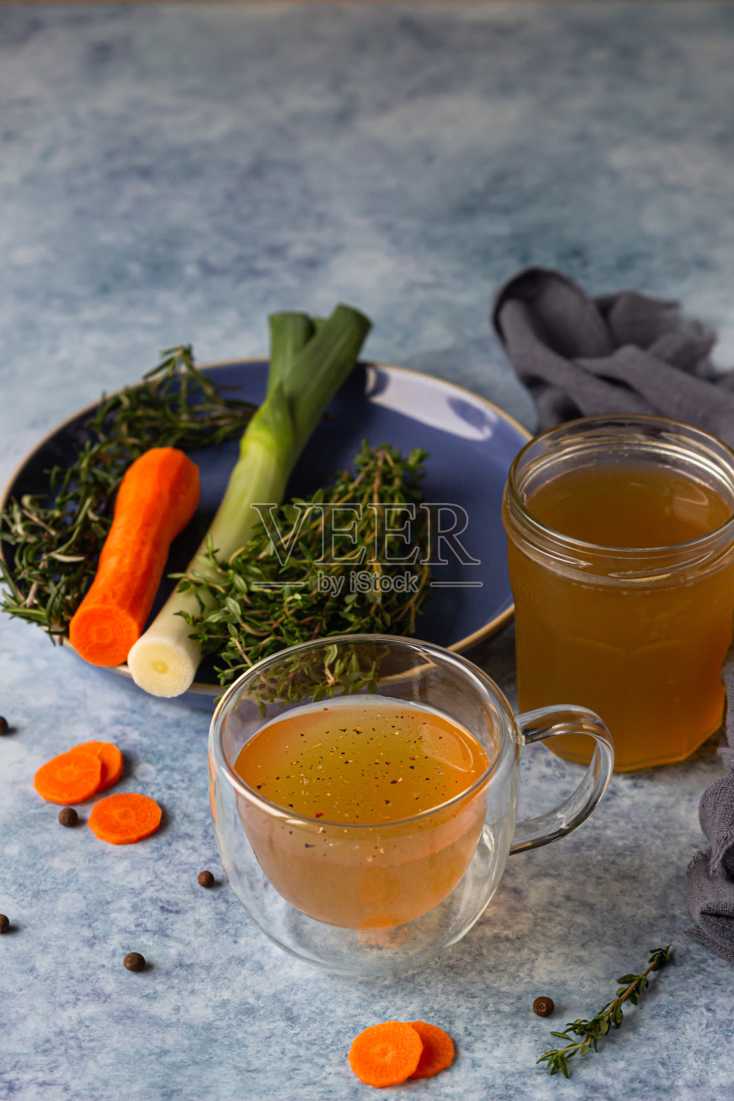 玻璃杯里自制骨汤配蔬菜,蓝色混凝土背景。胶原蛋白是人体的来源。照片摄影图片