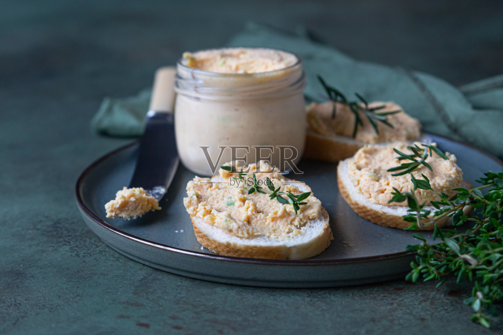 三明治熏鲑鱼和软奶油芝士馅饼或慕斯与百里香和迷迭香在陶瓷盘子,绿色混凝土背景。照片摄影图片