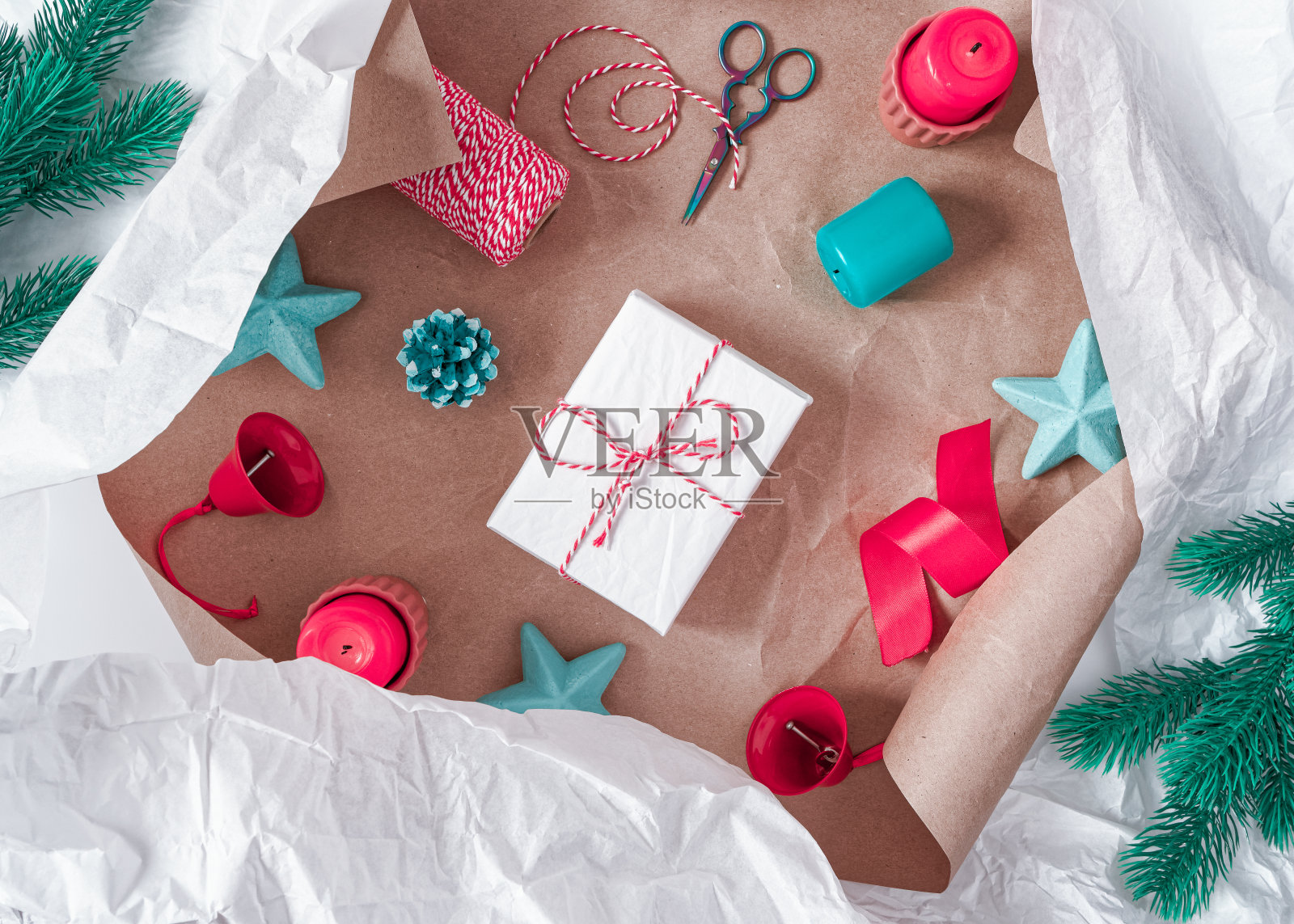 圣诞组成。礼物是用皱巴巴的白纸包装的。附近有一个彩绘的松果,蜡烛,铃铛,一卷线,剪刀,星星。礼品包装和准备的概念。照片摄影图片