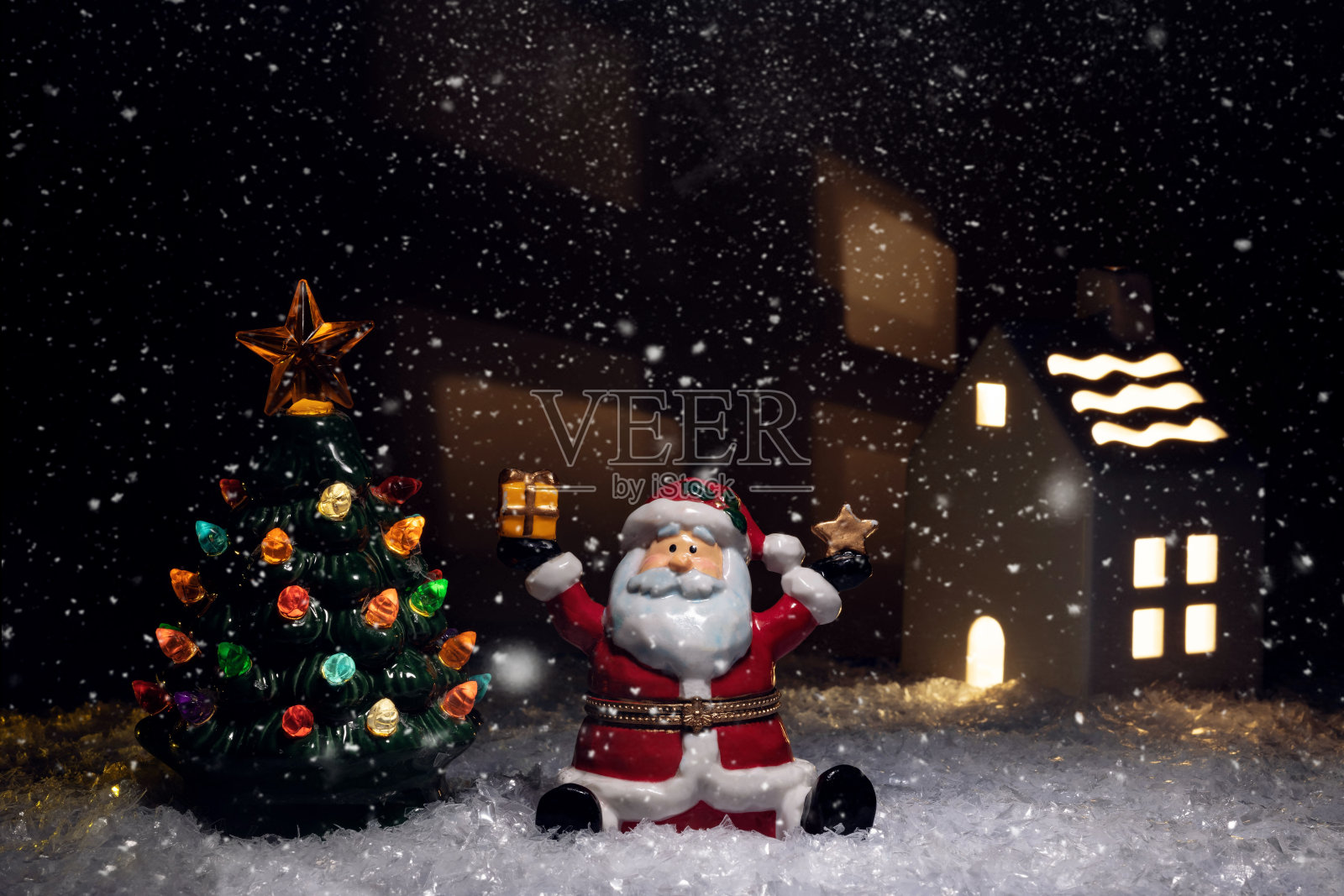 一个陶制的圣诞老人雕像坐在雪地里,旁边是一棵发光的陶制圣诞树照片摄影图片