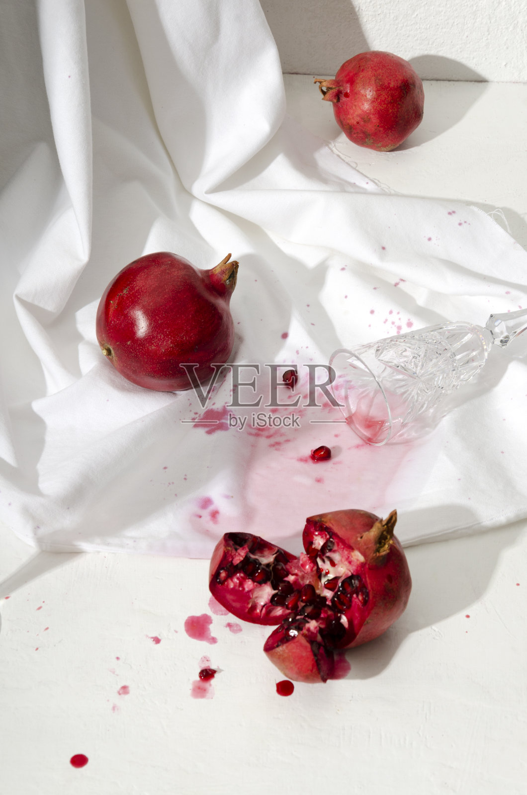 垂直的图像。去皮的石榴,两个完整的一个,从玻璃杯里把鸡尾酒洒在白色桌布上照片摄影图片