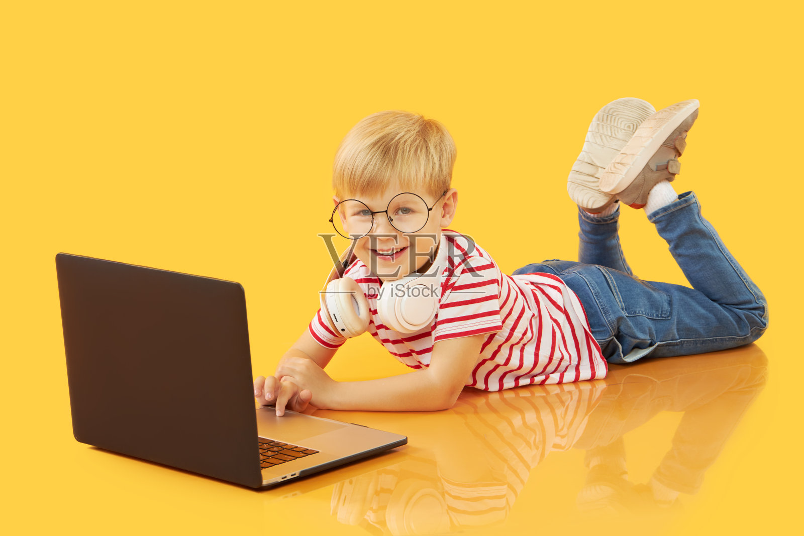 一个小男孩用黄色背景的笔记本电脑。教育,在线学习,在家学习,远程学习。隔离期间的小学生照片摄影图片