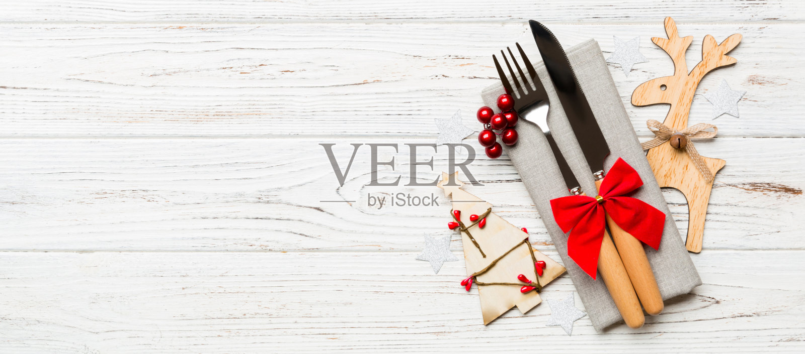 新年横幅上的餐巾纸上的刀叉。圣诞装饰品和木制背景上的驯鹿俯视图。假日家庭晚餐概念与空空间为您设计照片摄影图片