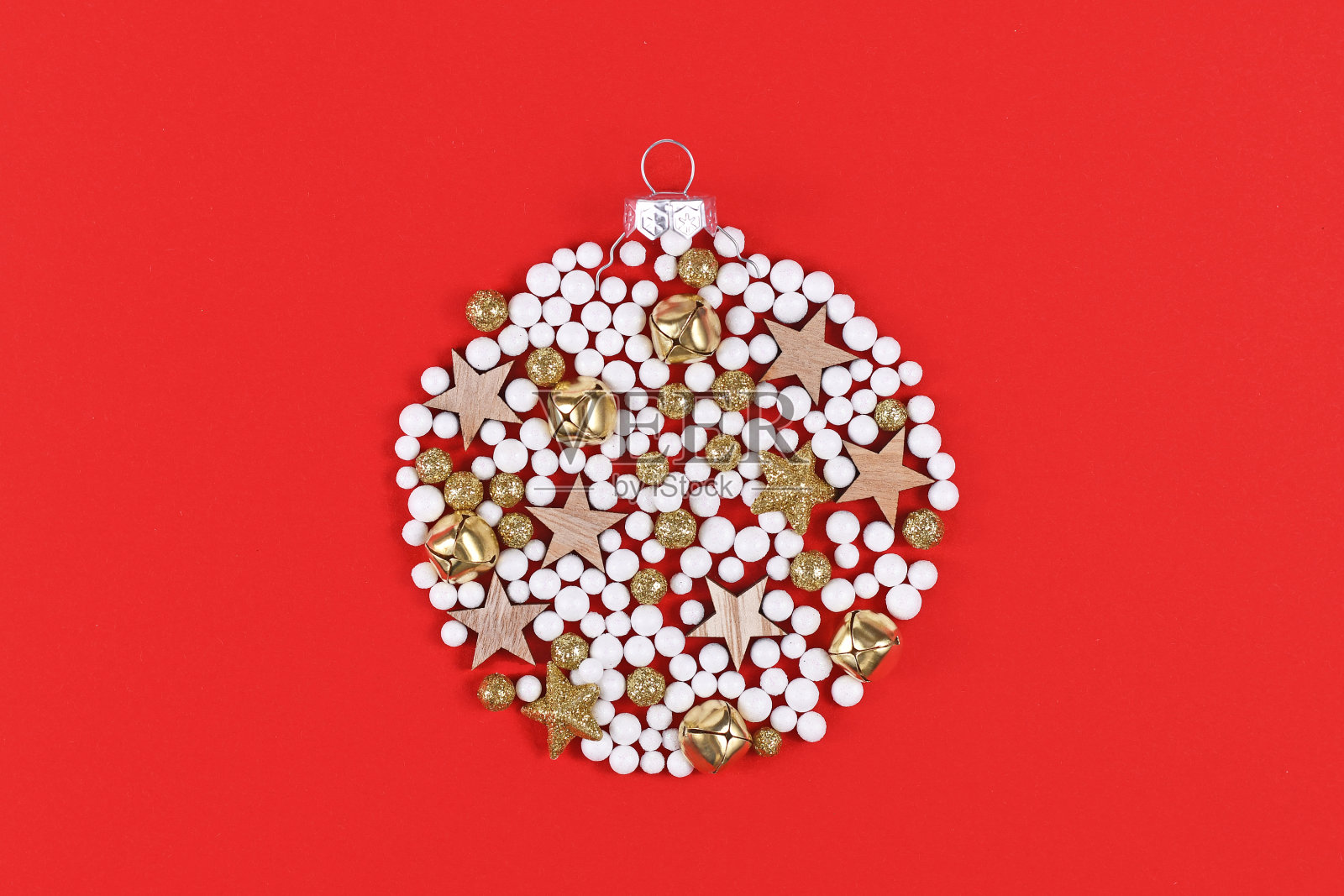 金色的铃铛,白色和金色的雪球和木制的星星装饰品在红色的背景上形成圆形的圣诞树装饰品照片摄影图片