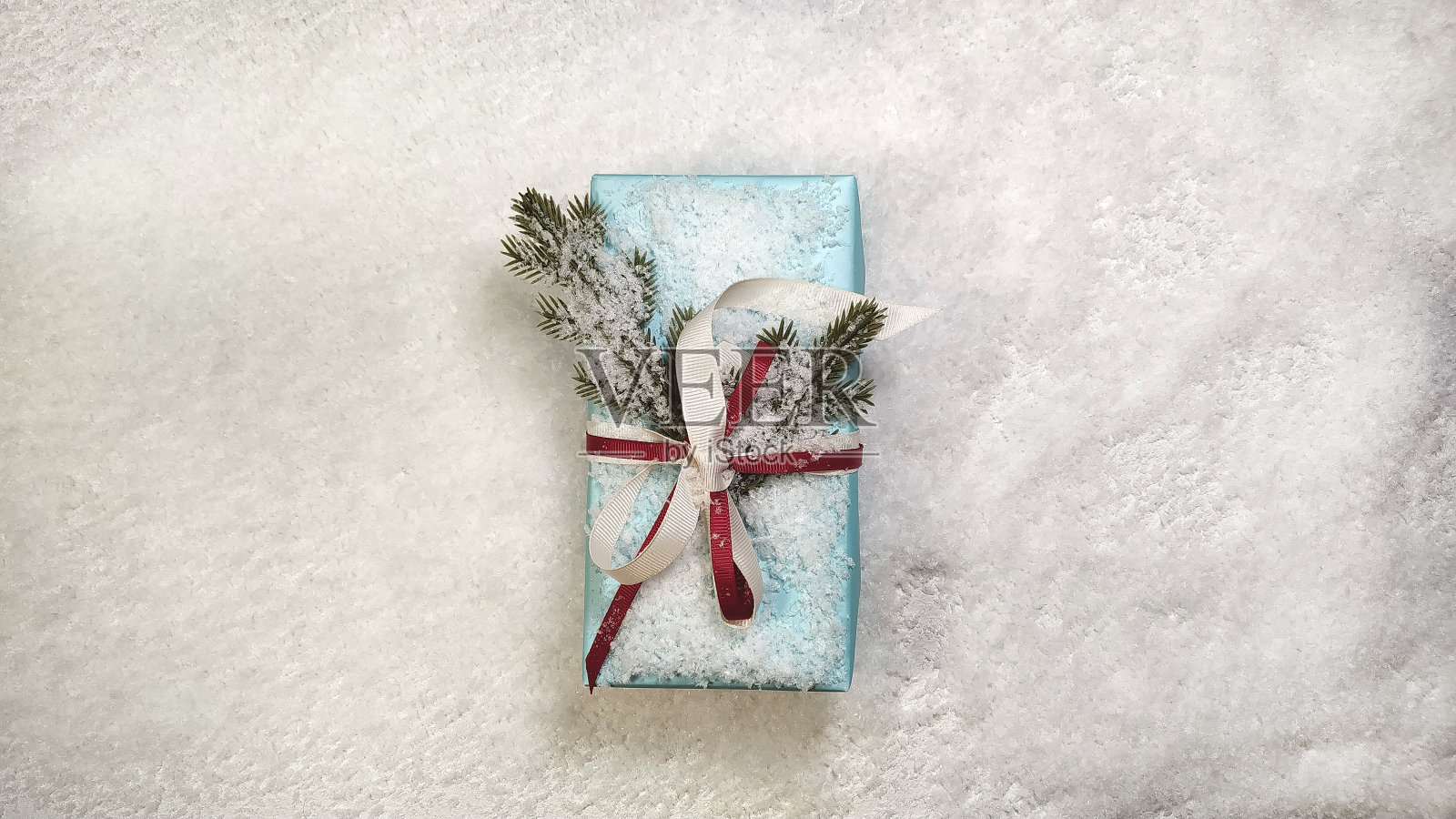 蓝色的圣诞礼盒在石头背景的雪与丝带和圣诞树的树枝。顶部视图与空间的文字和广告照片摄影图片