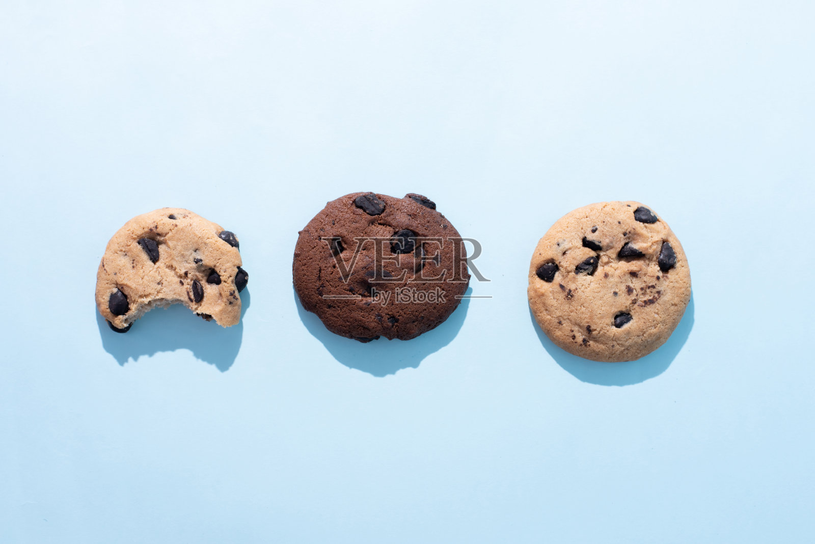 三个巧克力曲奇,一个在蓝色背景上被咬了。照片摄影图片
