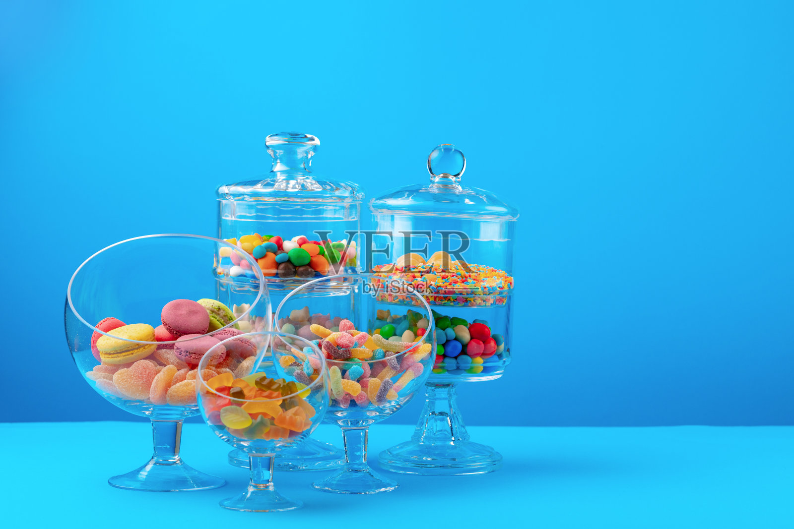 蓝色背景下的彩色糖果玻璃容器照片摄影图片