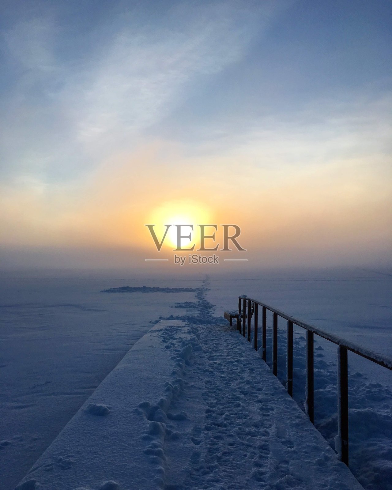 森林湖上的日落。一条沿着积雪覆盖的人行天桥延伸到远处的小路照片摄影图片