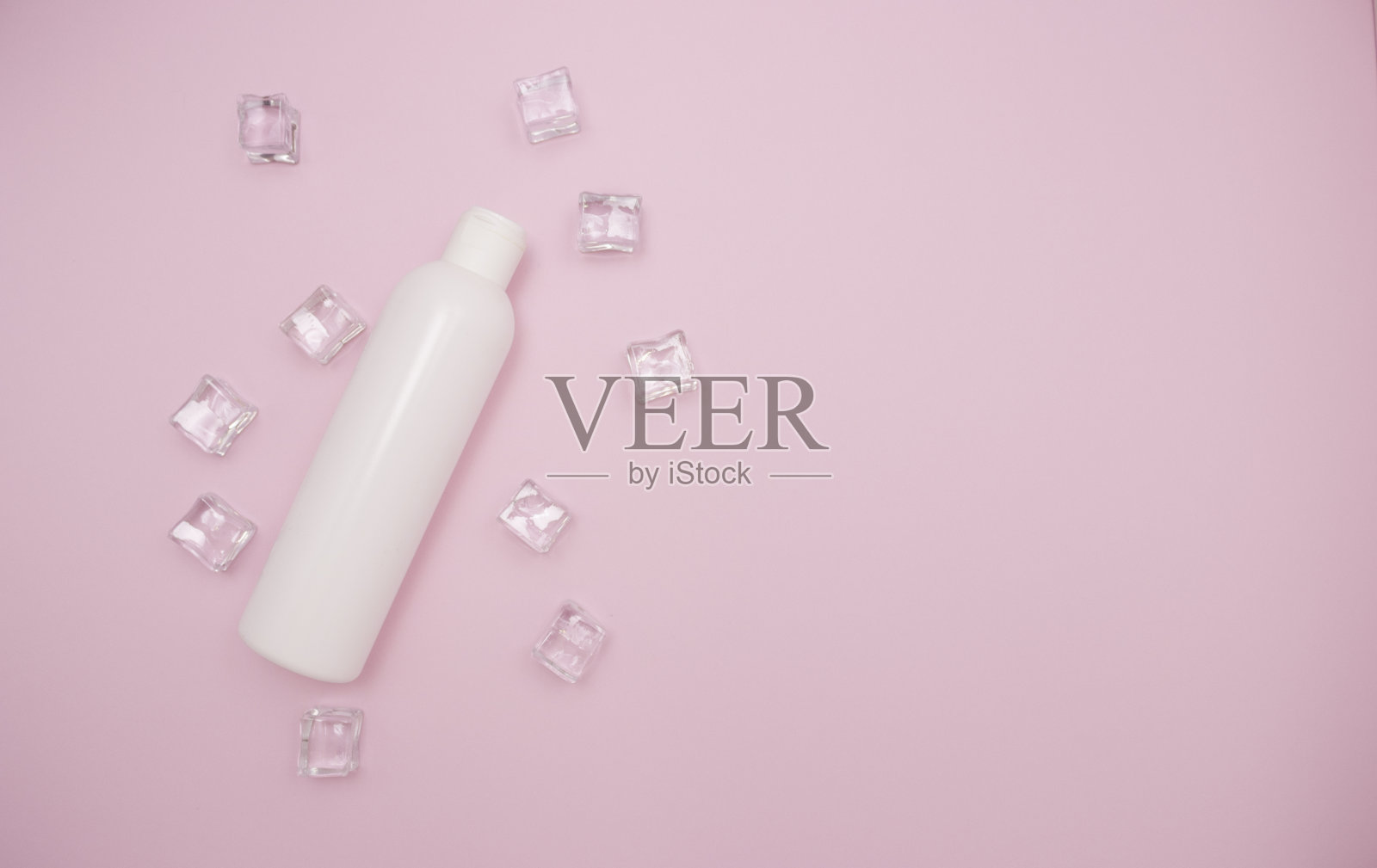 白色塑料瓶洗发水或其他化妆品。冰块周围,粉色背景,自由的文字空间,俯视图。照片摄影图片