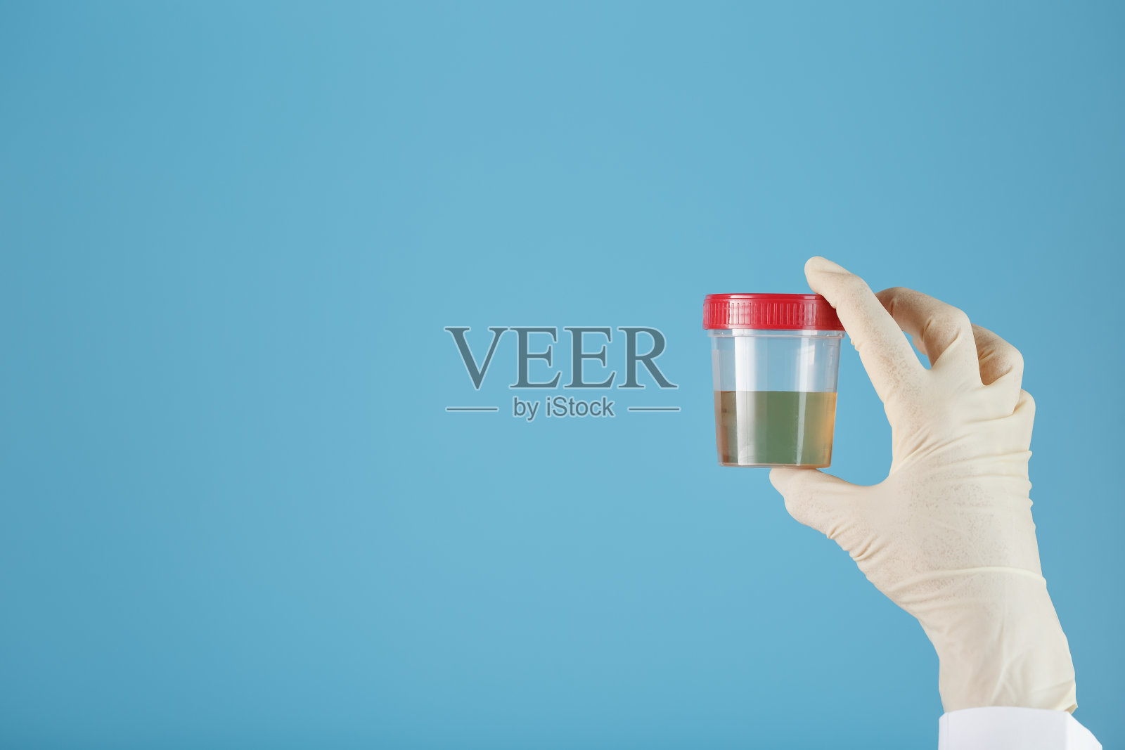 一个生物材料的容器和尿液分析在一个医生的手在白色橡胶手套在一个蓝色的背景。照片摄影图片