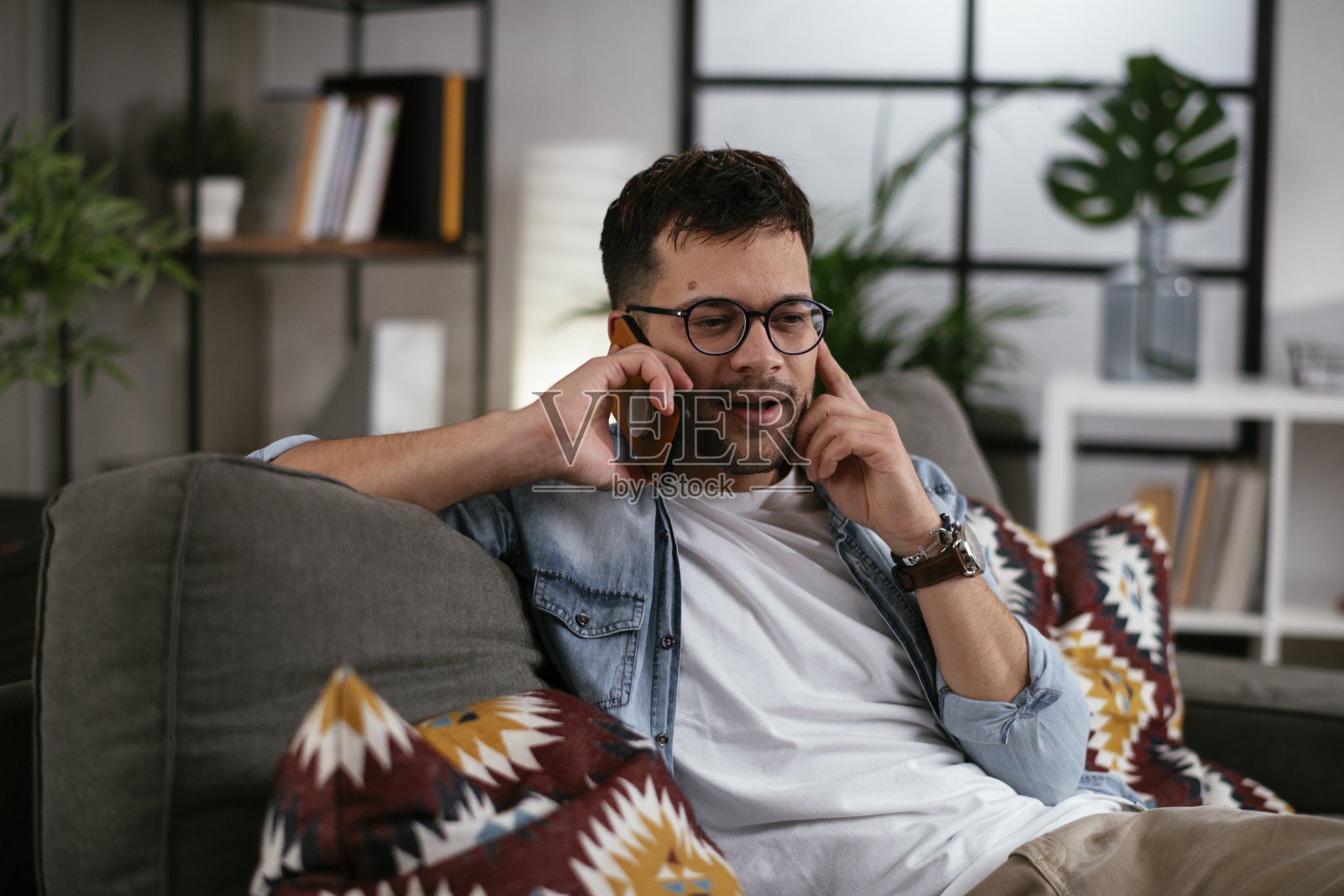 年轻人坐在沙发上打电话。照片摄影图片
