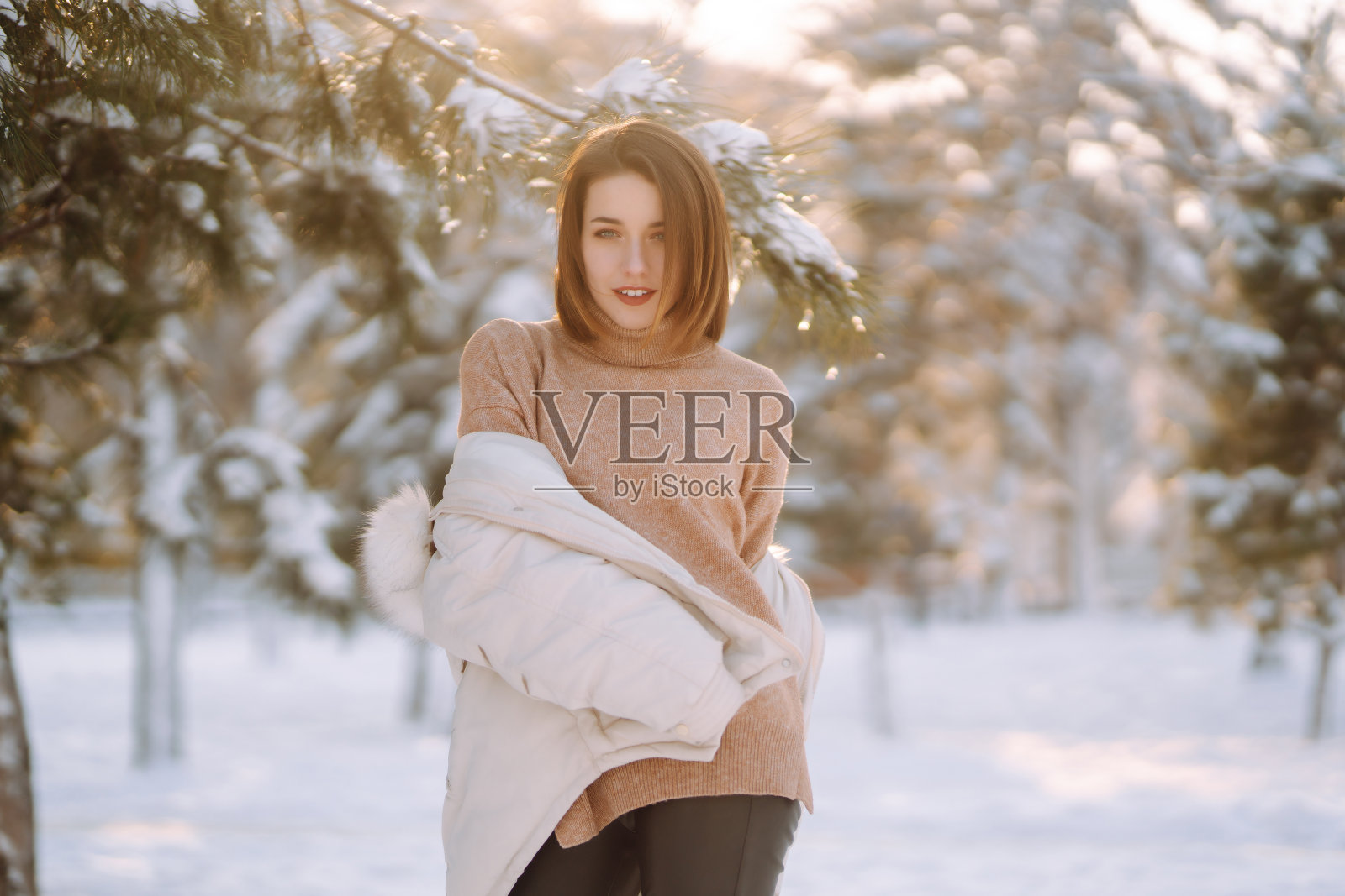 一个穿着冬装的漂亮女人在白雪覆盖的公园里摆姿势照片摄影图片