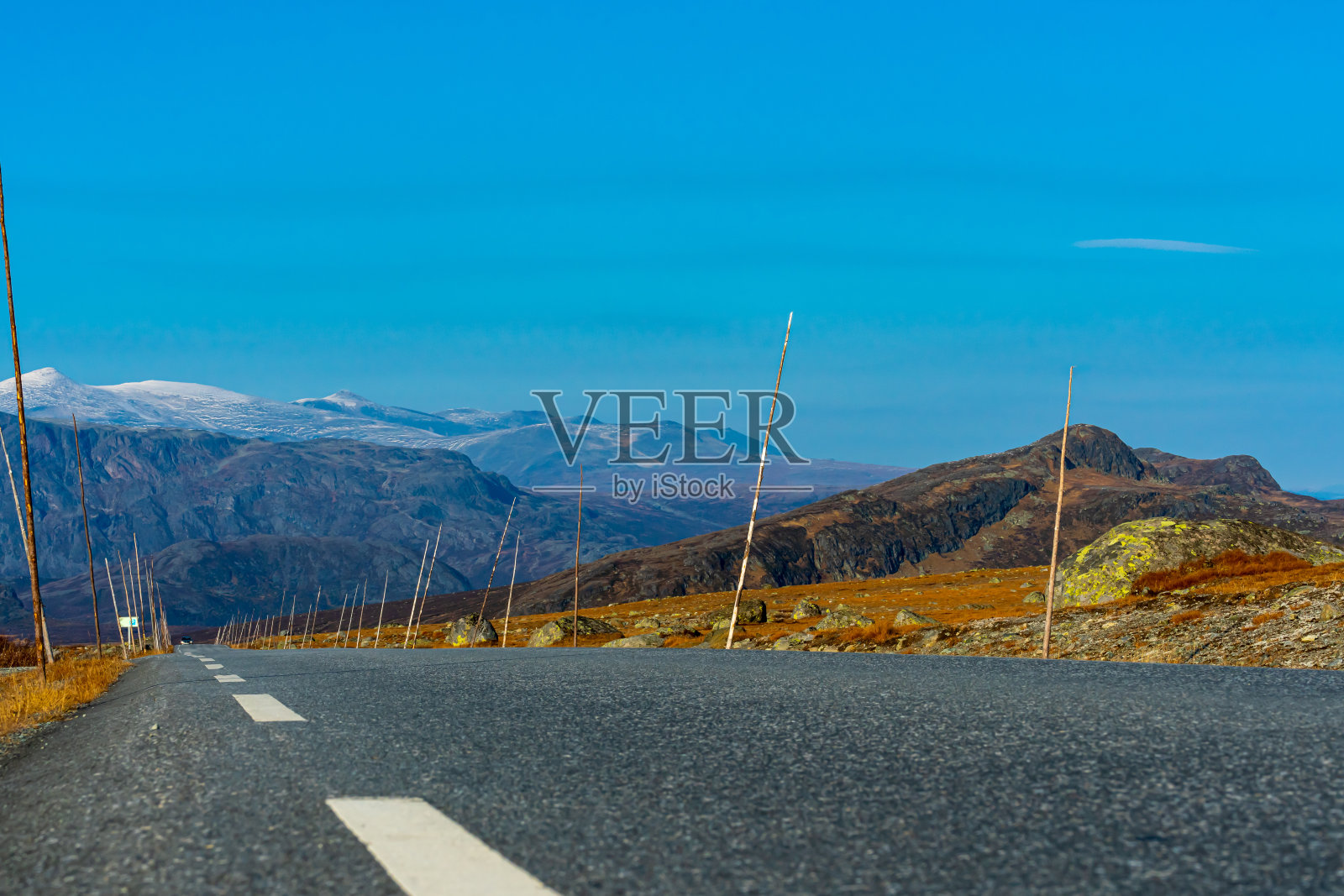 柏油路穿过高山高地,旁边放着高大的木棒标记。景深浅。照片摄影图片