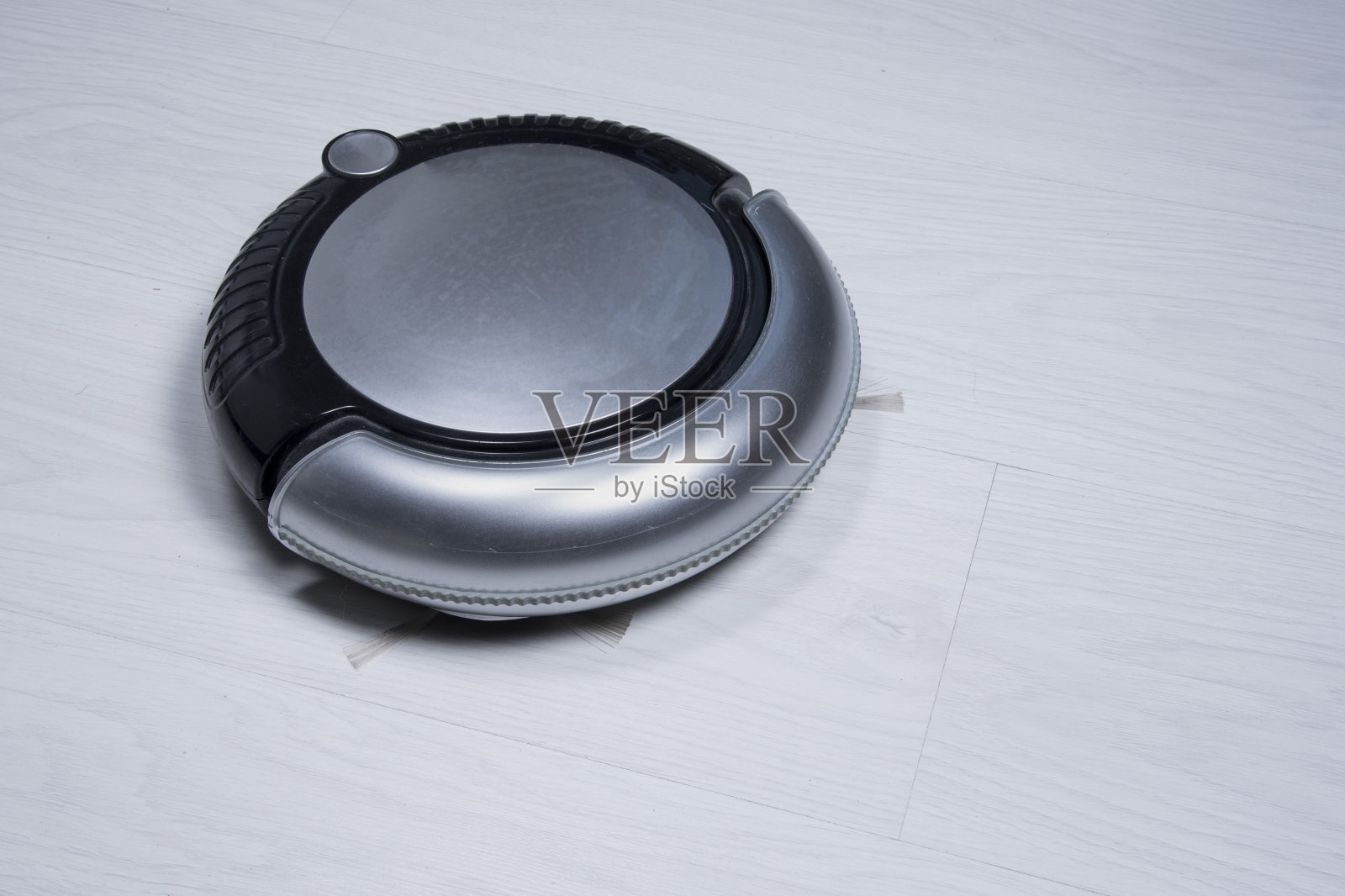 黑色和银色的机器人吸尘器在白色强化木地板上。智能家居。照片摄影图片