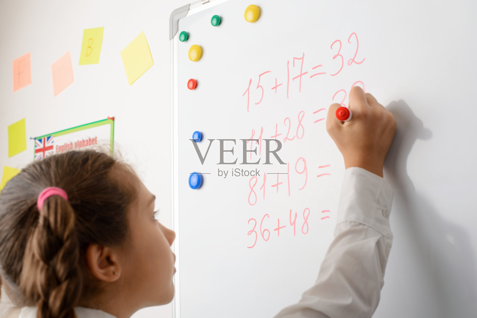 女学生在白板上计算数字,在学校上数学课,在黑板旁边展示她的知识照片摄影图片