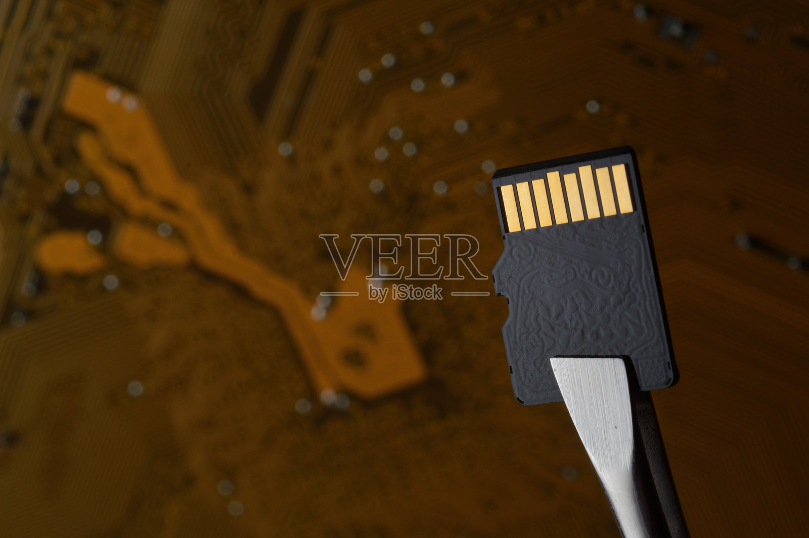 微型SD存储卡的特写,背景是一个微电路,夹着镊子。照片摄影图片