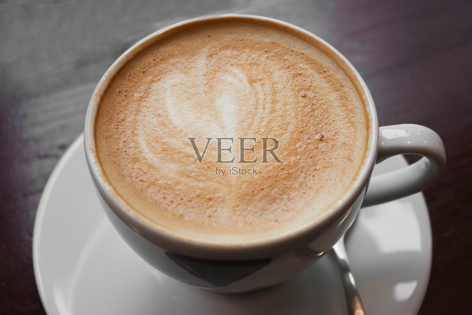 桌上的白杯子里放着一杯带泡沫的咖啡照片摄影图片