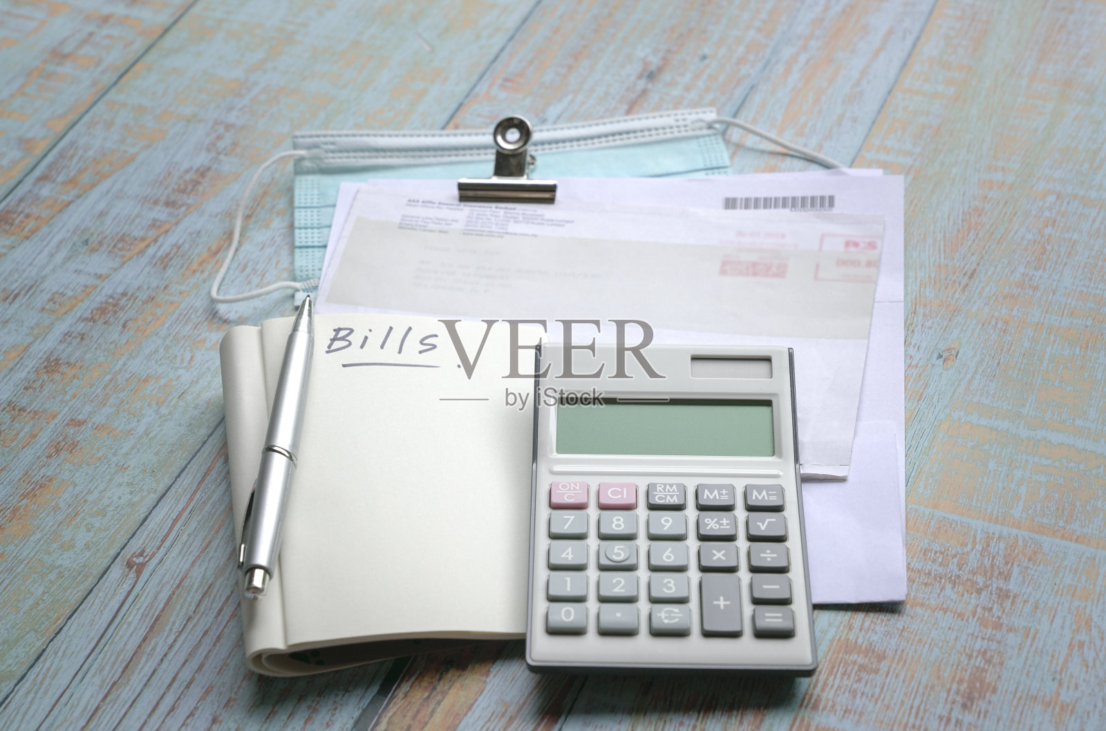 木桌上放着账单、计算器、记事本和口罩。大流行期间的危机概念。照片摄影图片