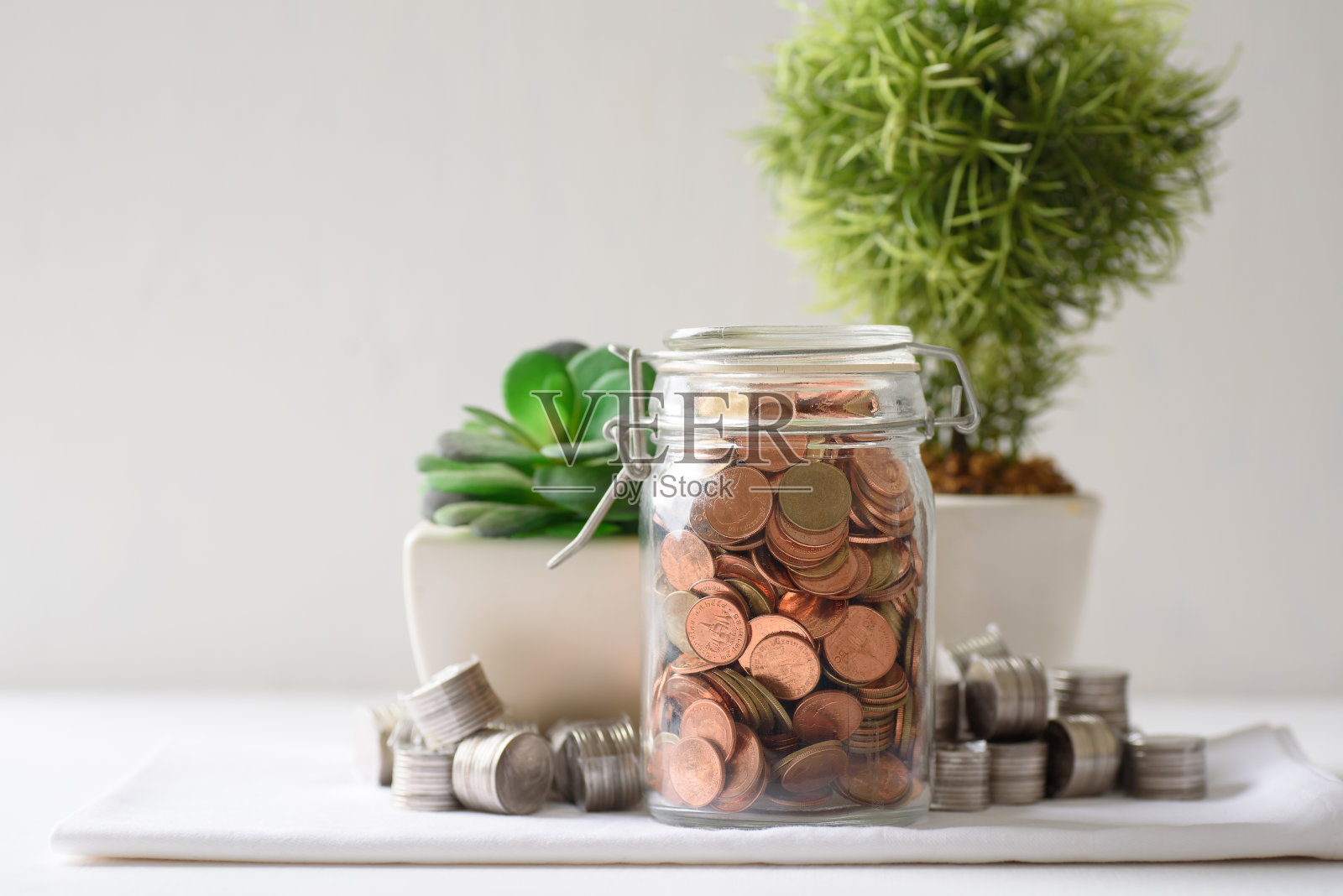 在玻璃容器和装饰植物中的硬币。照片摄影图片