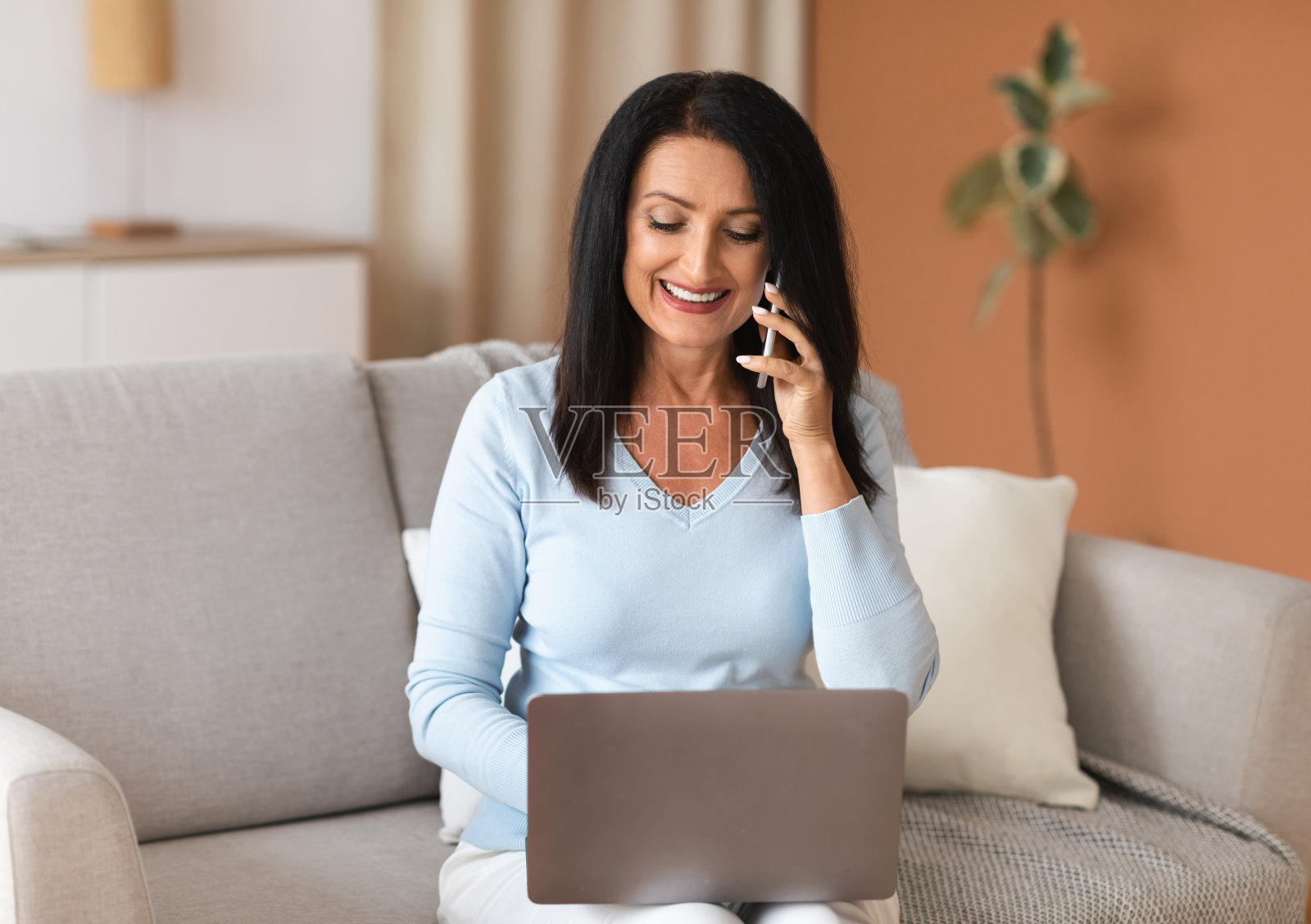 微笑成熟的女人用笔记本电脑在智能手机上聊天照片摄影图片