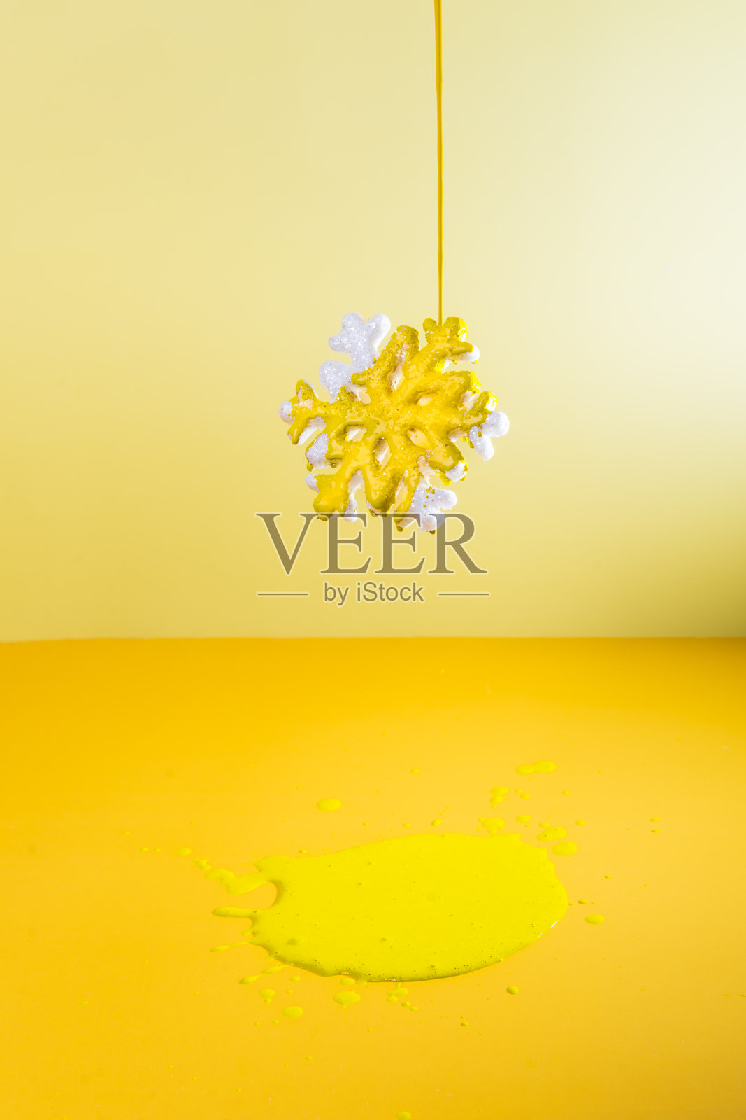 明亮的黄色油漆倒在悬挂在空中的雪花上。它下面有一滩油漆。创意背景的2021年的颜色宣布。创造性的过程。垂直的名片。照片摄影图片