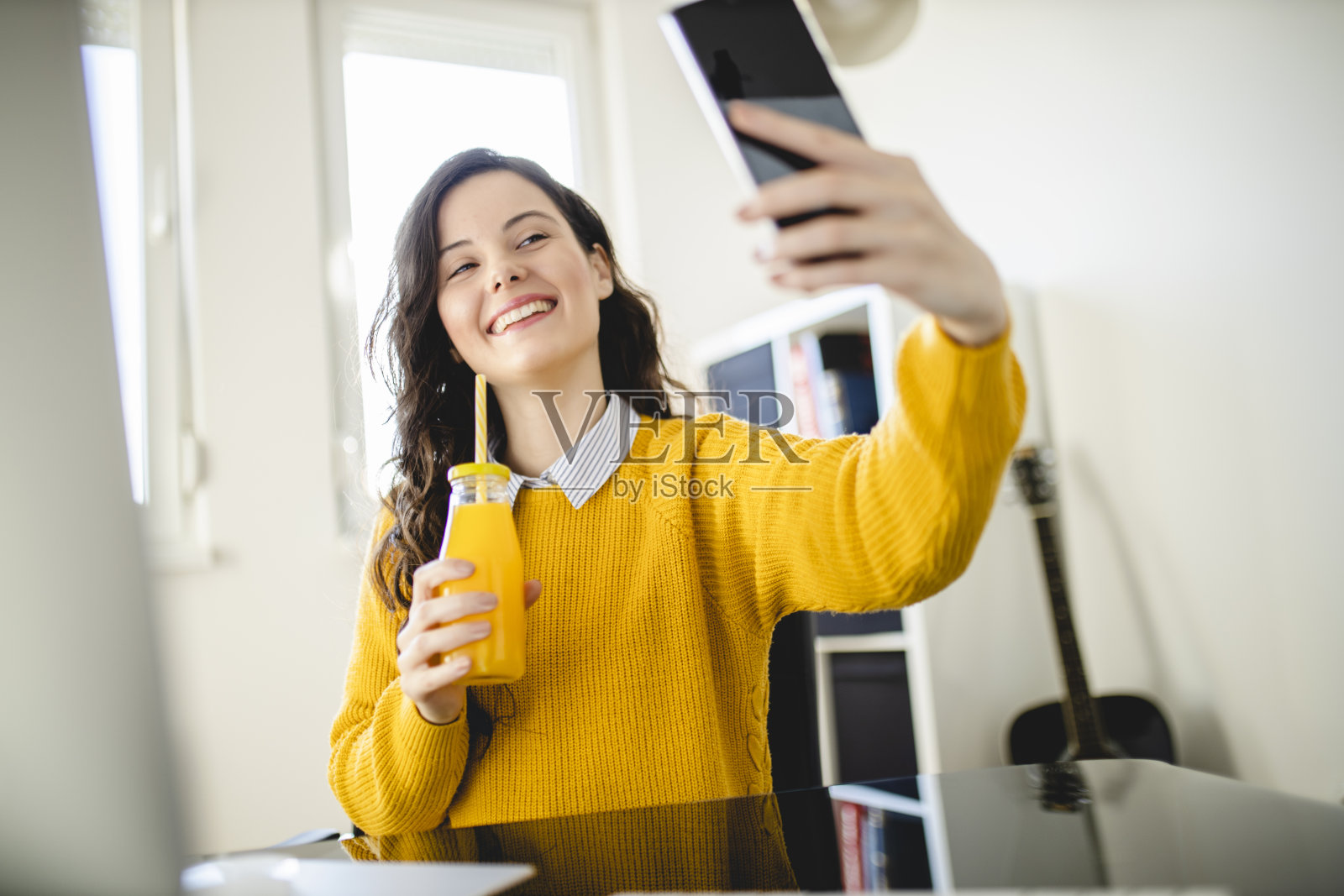 年轻的学生女孩喝果汁,在家里用手机照片摄影图片